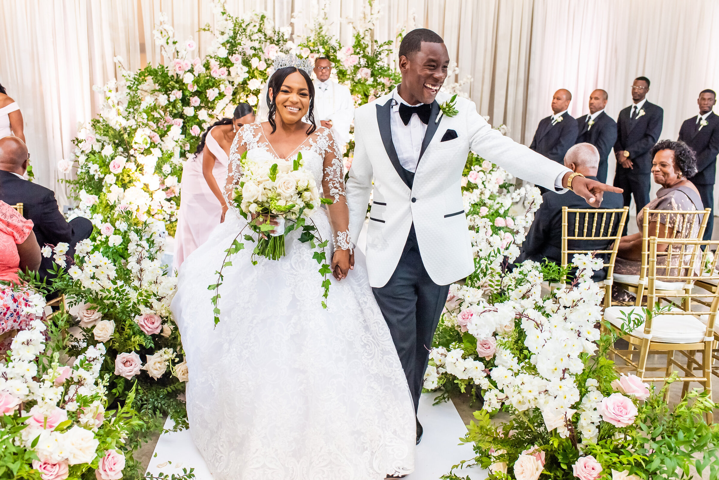 Bride and groom joyfully exit ceremony surrounded by pink and white florals, gold chairs, and family guests at a luxury Southern wedding in Birmingham styled by Wells Design Co