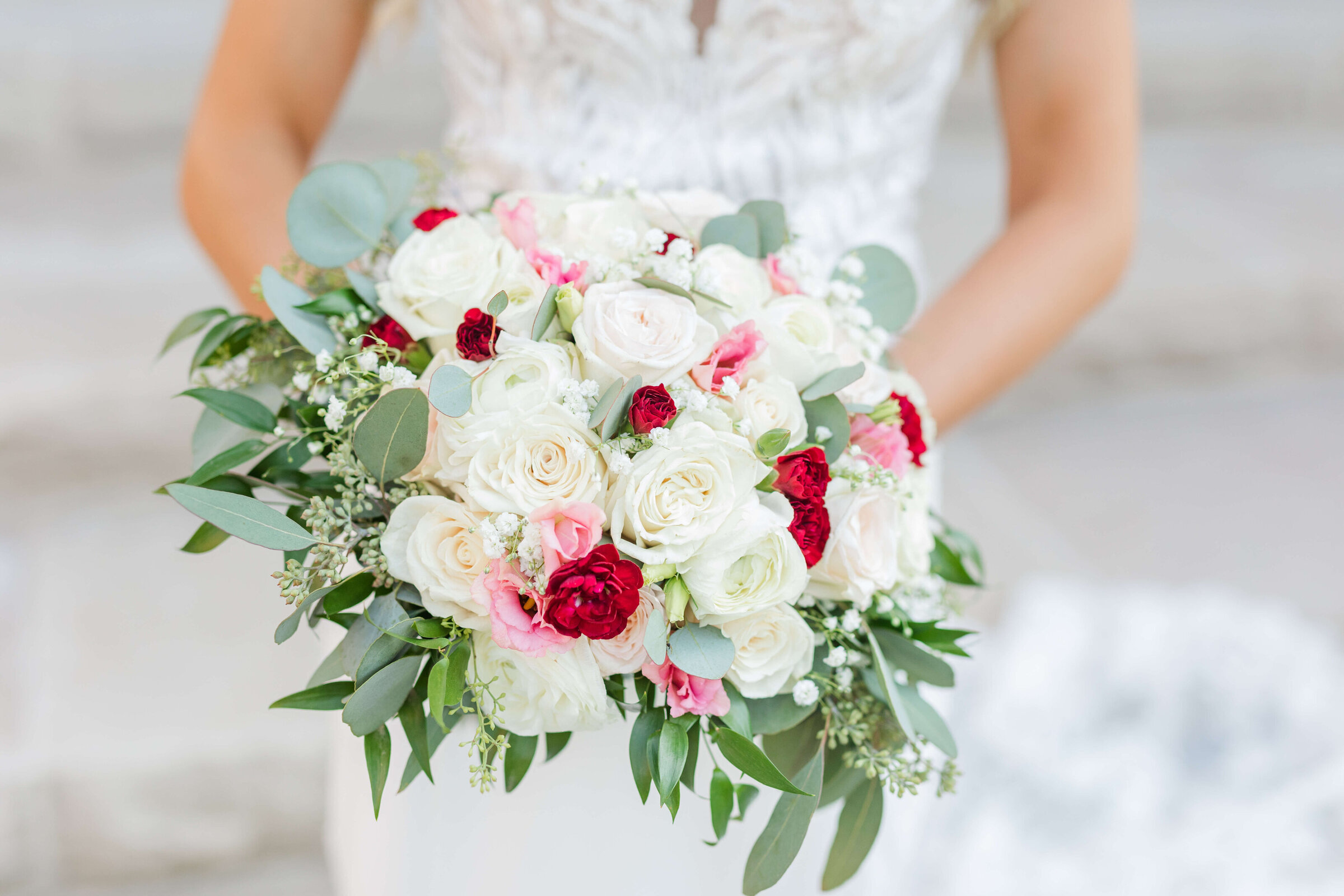 an up close photo of a bride holding a bouquet. The bouquet has red, white, and pink flowers. Taken by a Lexington wedding photographer