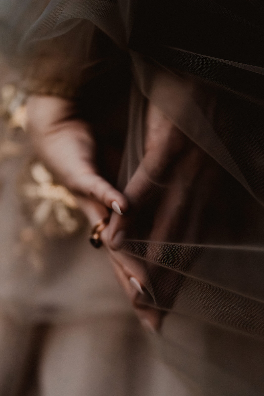 a detail shot of two hands pressing towards each other, a veil of thin fabric between them stretching lightly in the wind