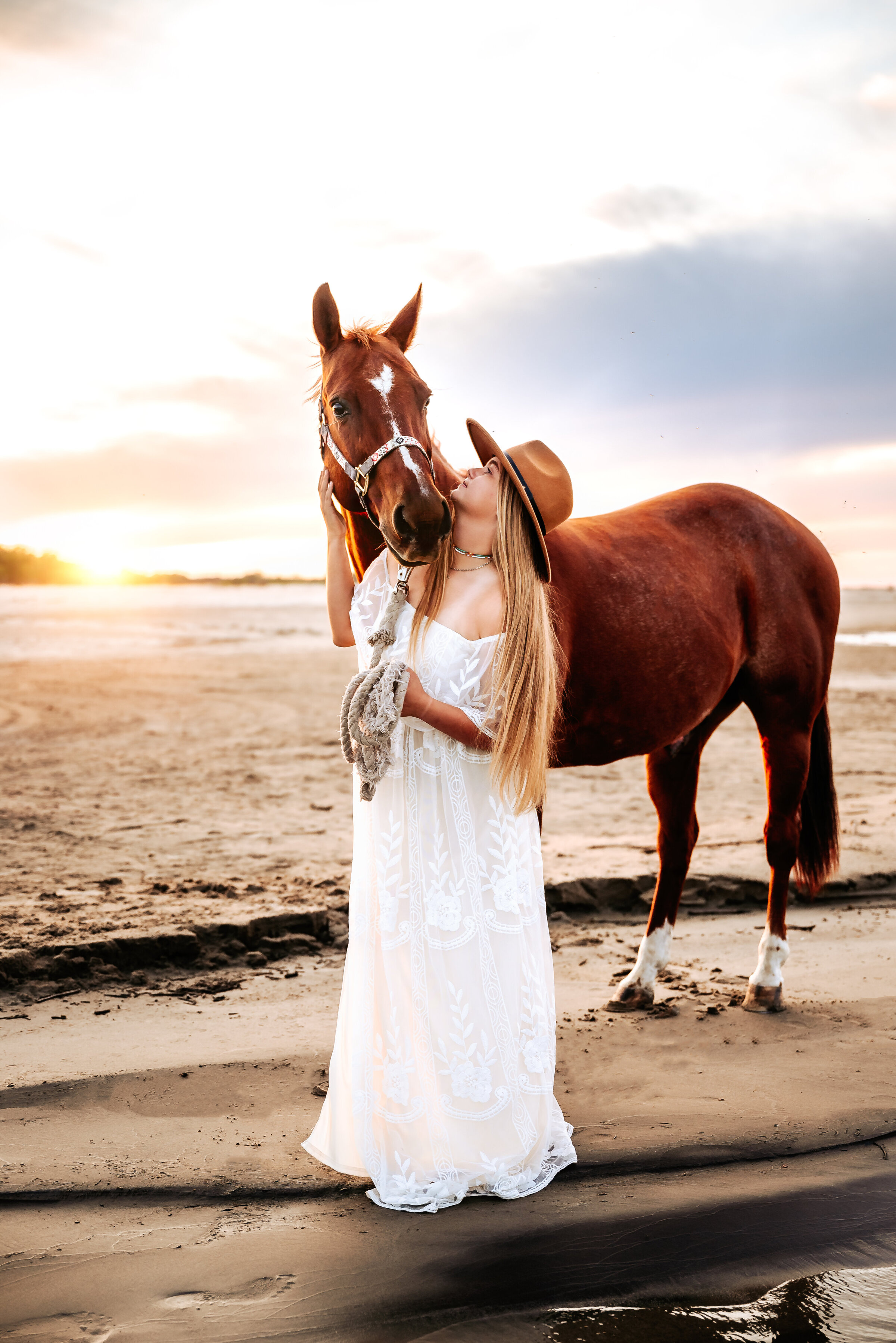 senior girl looks up at her horse on the beach in a white flowy dress