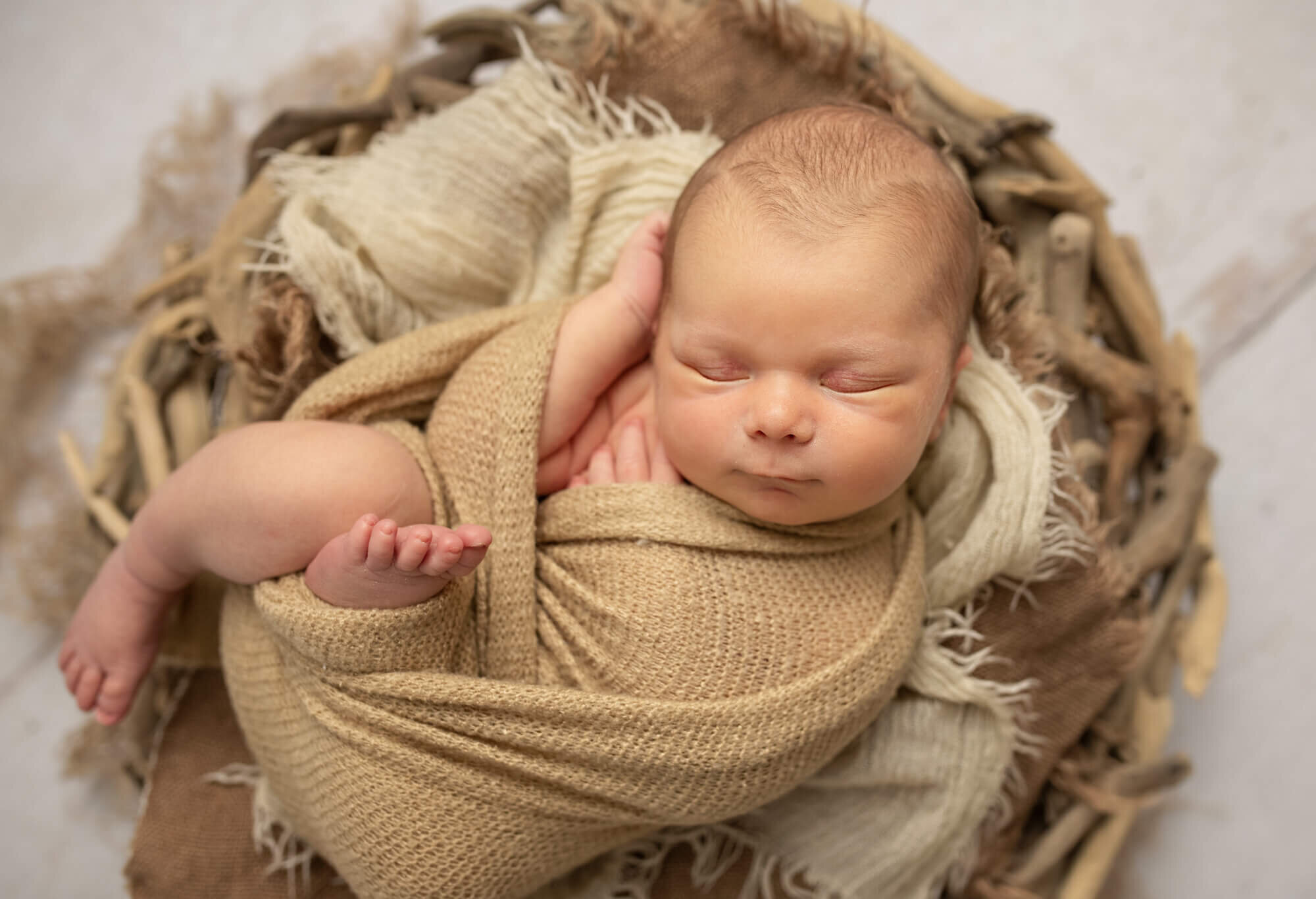 Newborn baby boy in beige wrap in relaxed pose with foot dangling