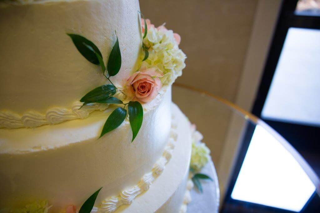 Close up of the side of a wedding cake. It's a white three layer cake with flowers on the side. The photo shows the right side of the cake and the glass table it sits on. Photo by wedding photographer sacramento, ca.