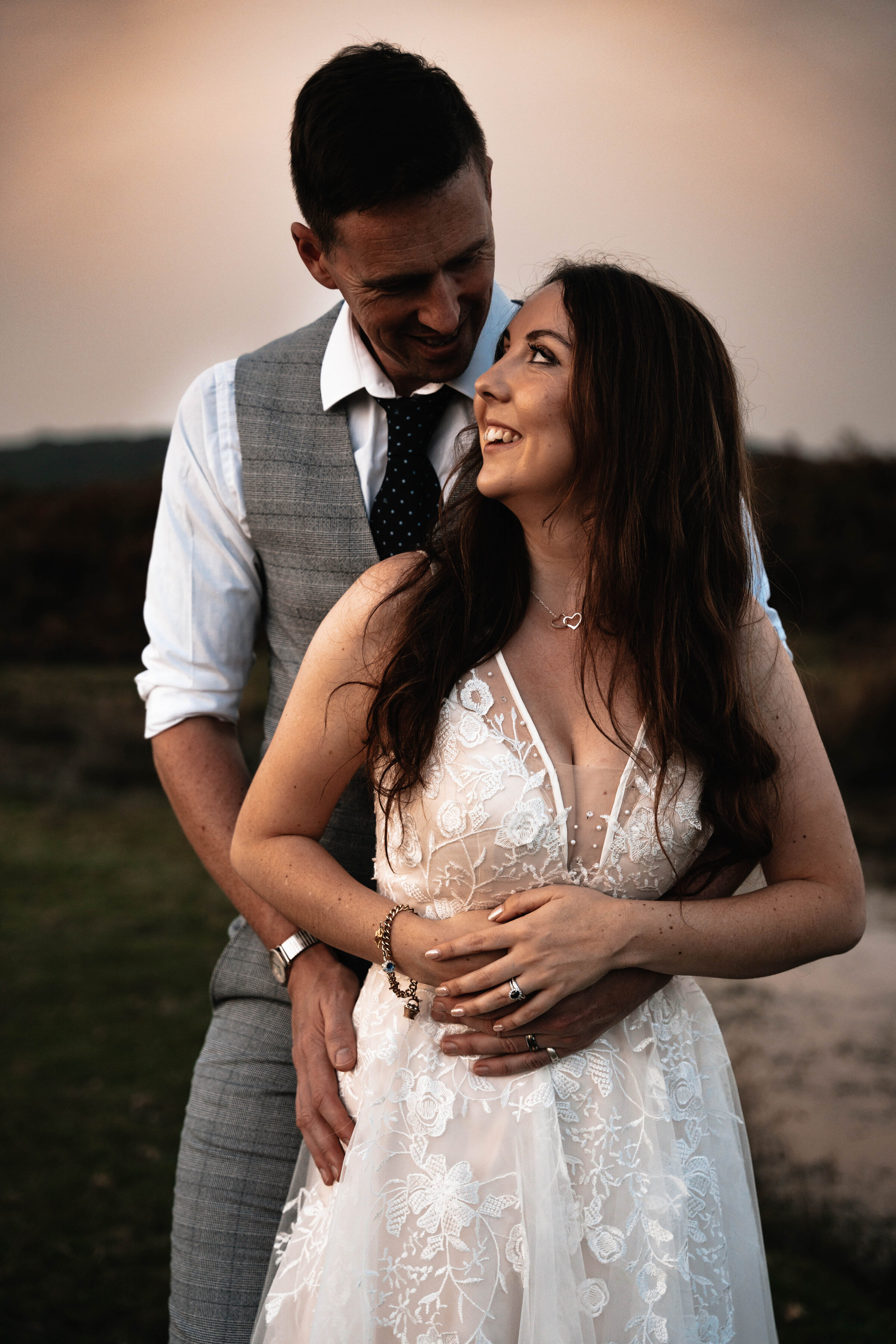 Bride and Groom in wedding attire smiling and embracing with golden sunset in background