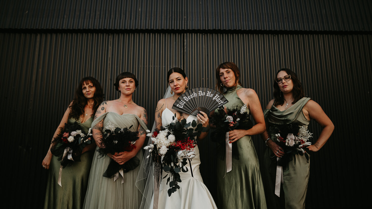 Alternative Tattooed bride and her bridesmaids in front of  a black metal barn.