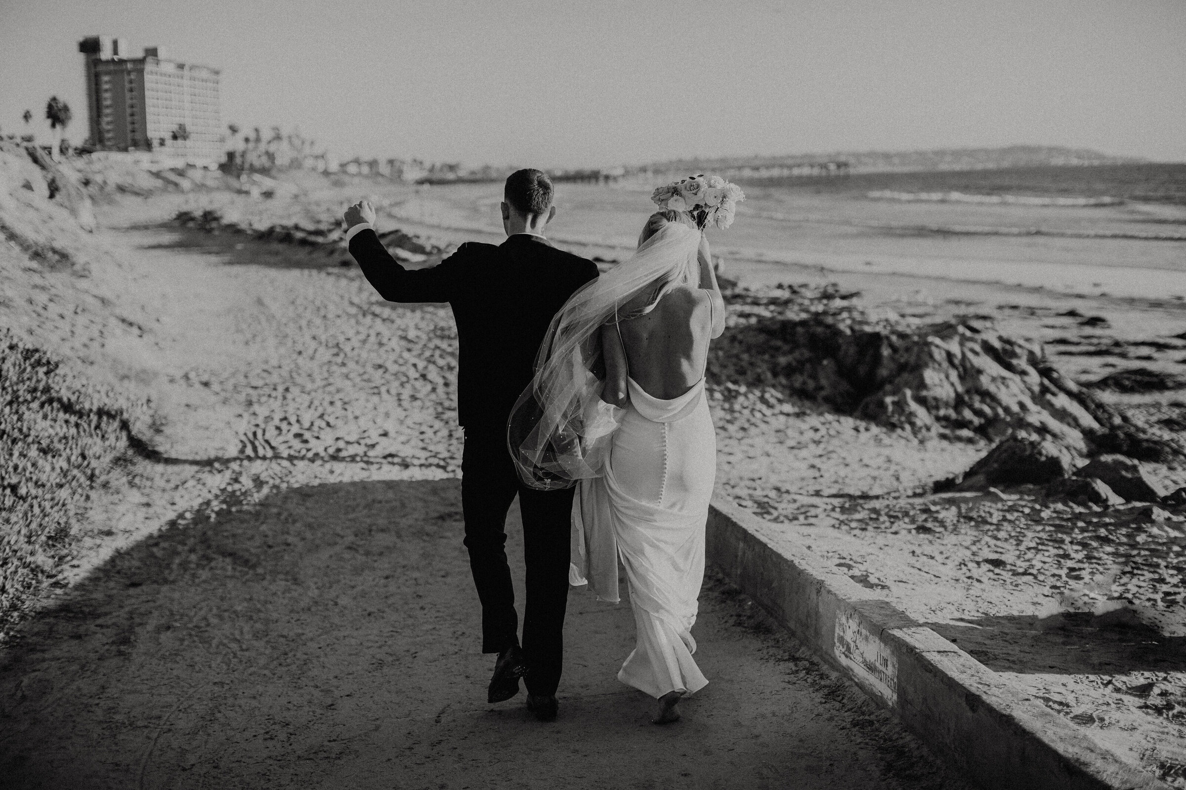 black and white photo of a couple walking on the beach to take photos after getting married.