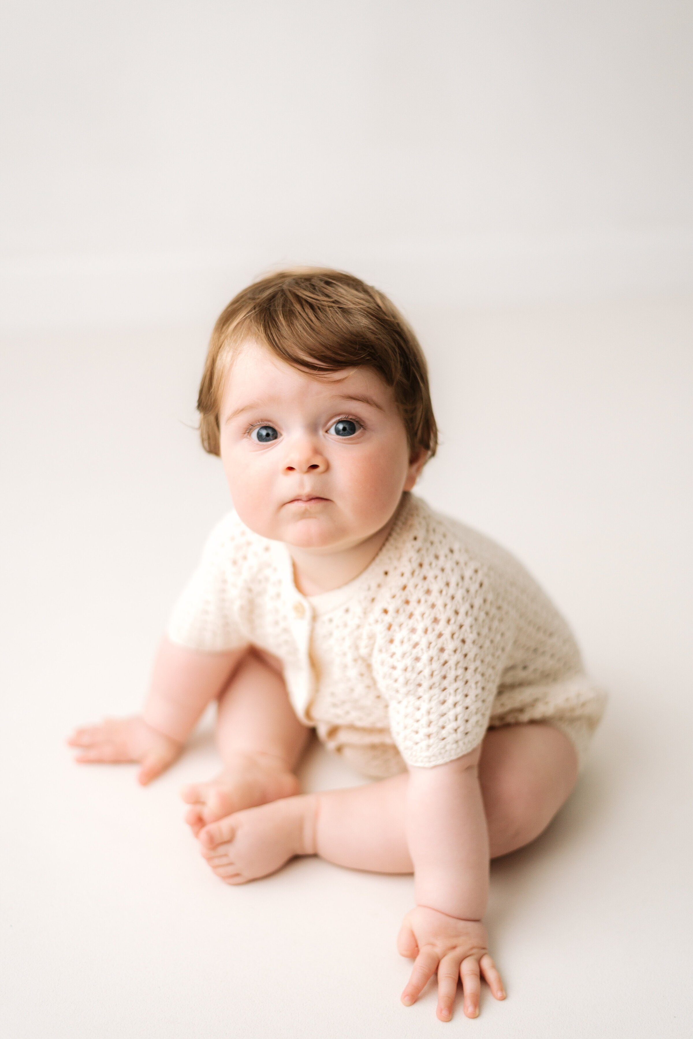 Little boy sitting on white floor at milestone photoshoot in Billingshurst