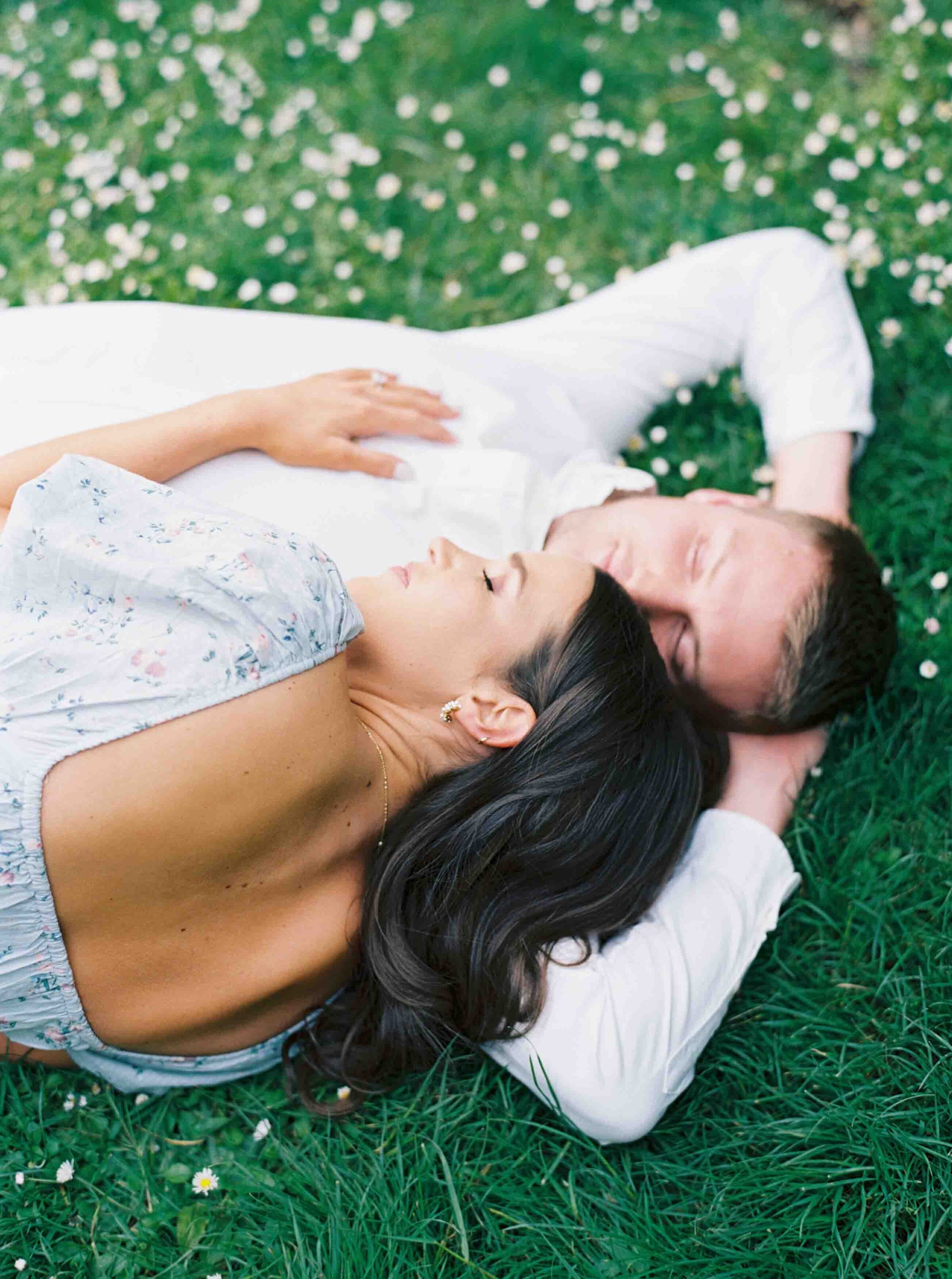 couple laying in grass on each other with eyes closed relaxing