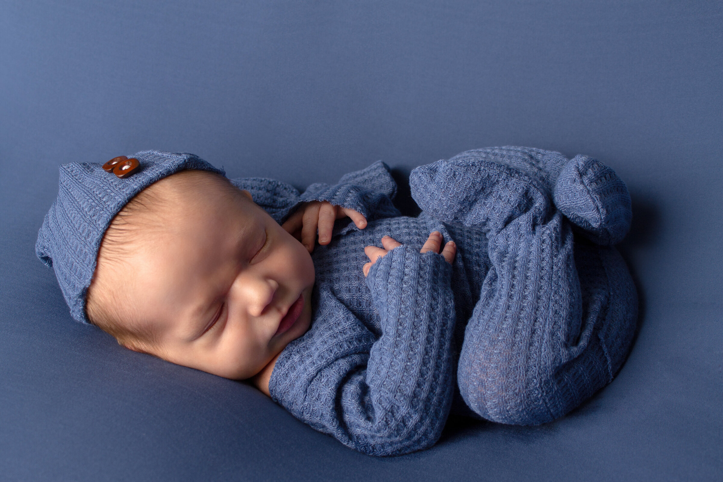 Minot, North Dakota newborn  laying on his back in all blue.