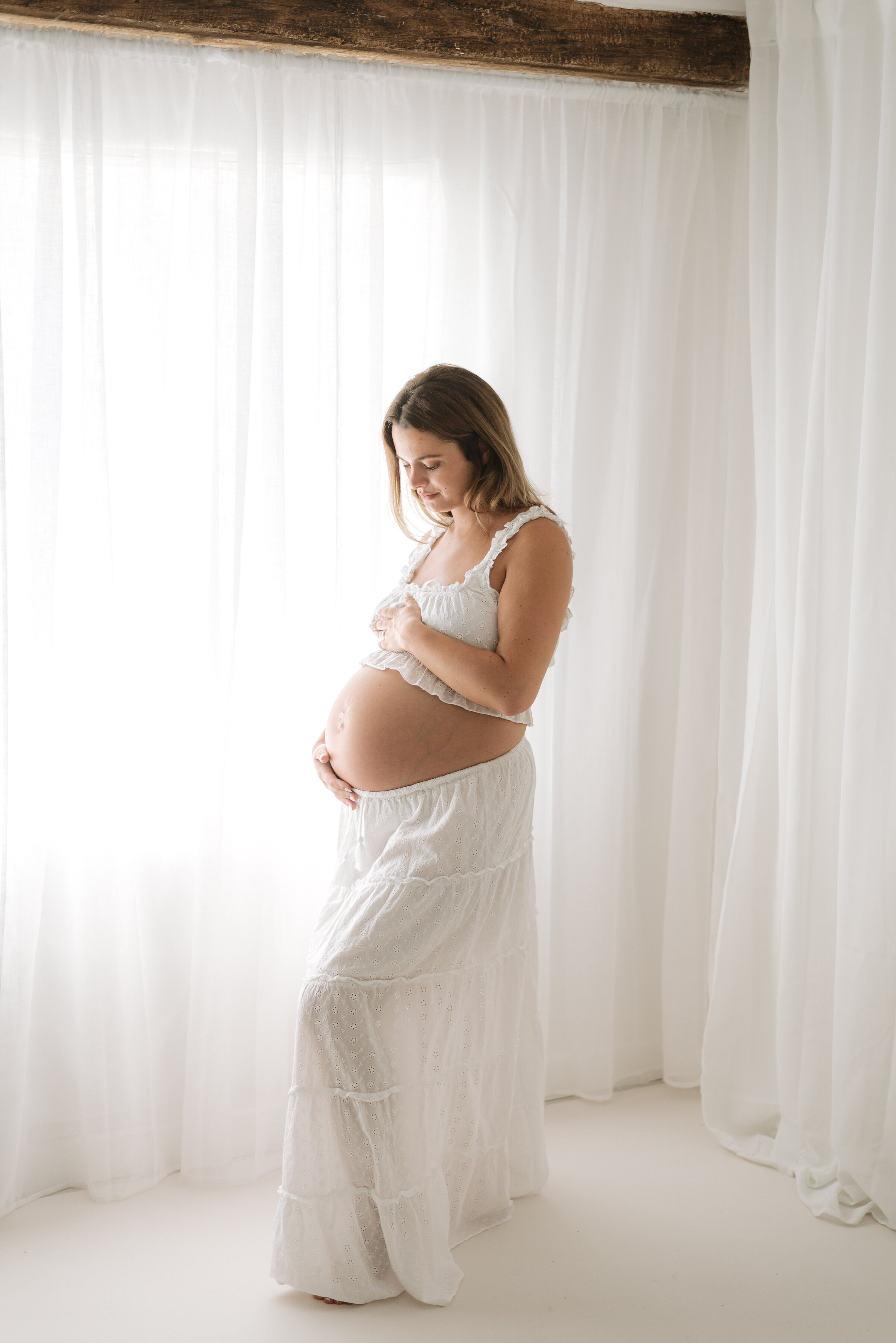 A pregnant mother standing up looking down at her belly at Billingshurst maternity photoshoot