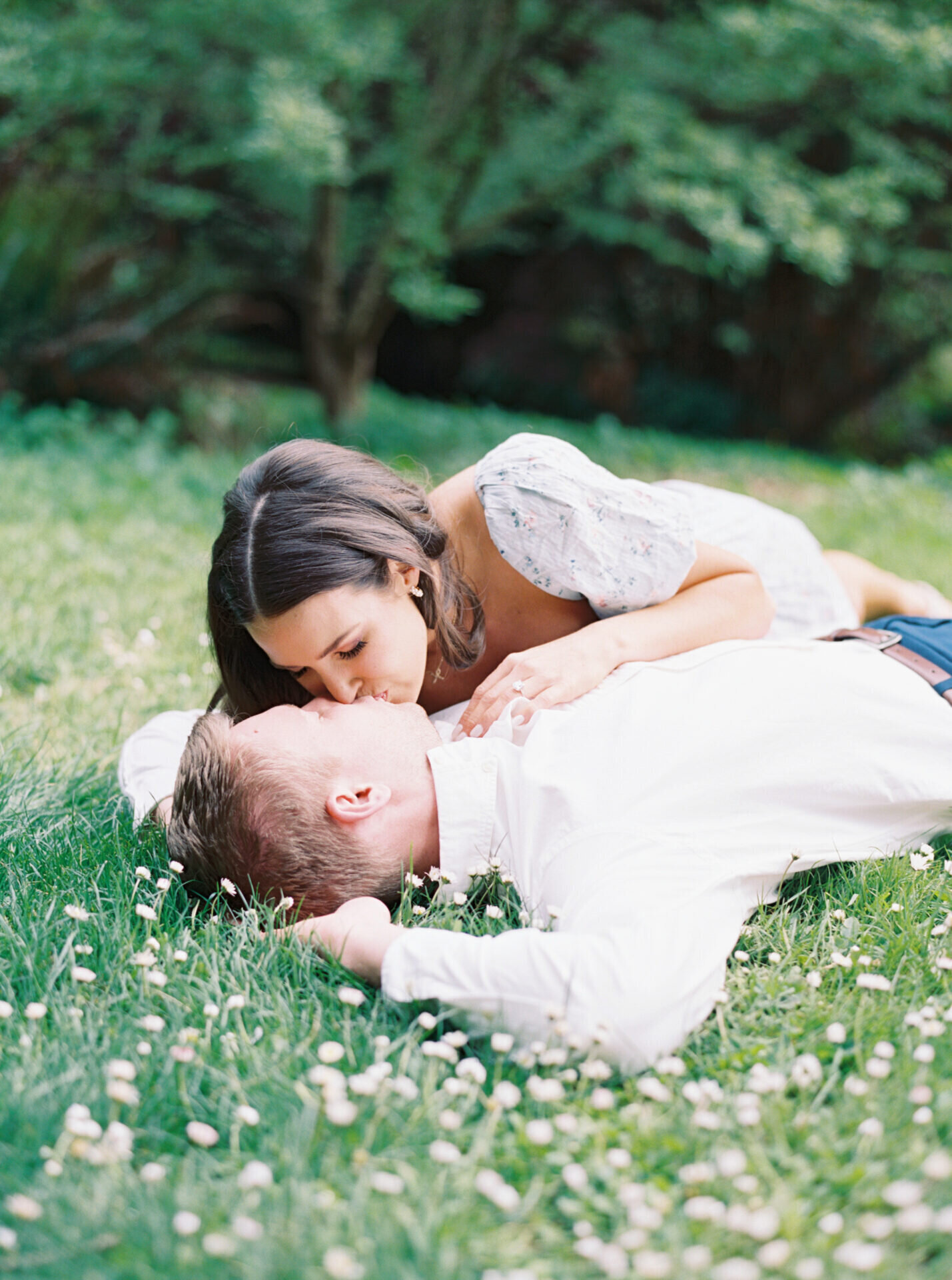 couple kissing as they lay in the grass and white flowers