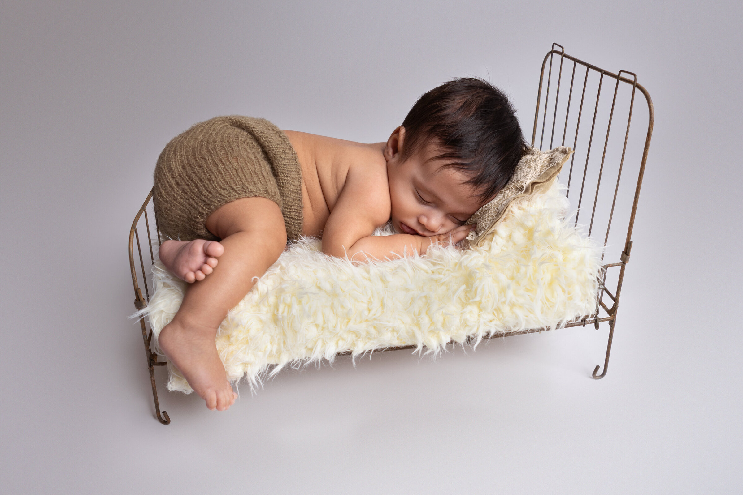 Little boy in brown shorts, curled up on a metal bed in Minot, ND studio.
