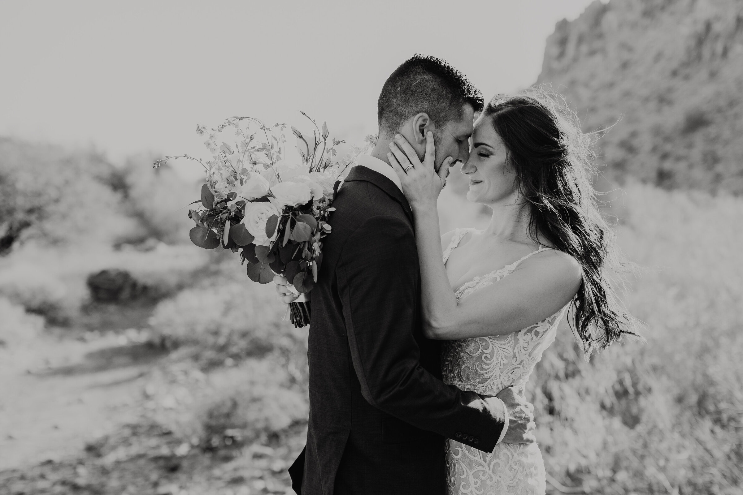 Black and white image of a husband and wife embracing in the wind after getting married