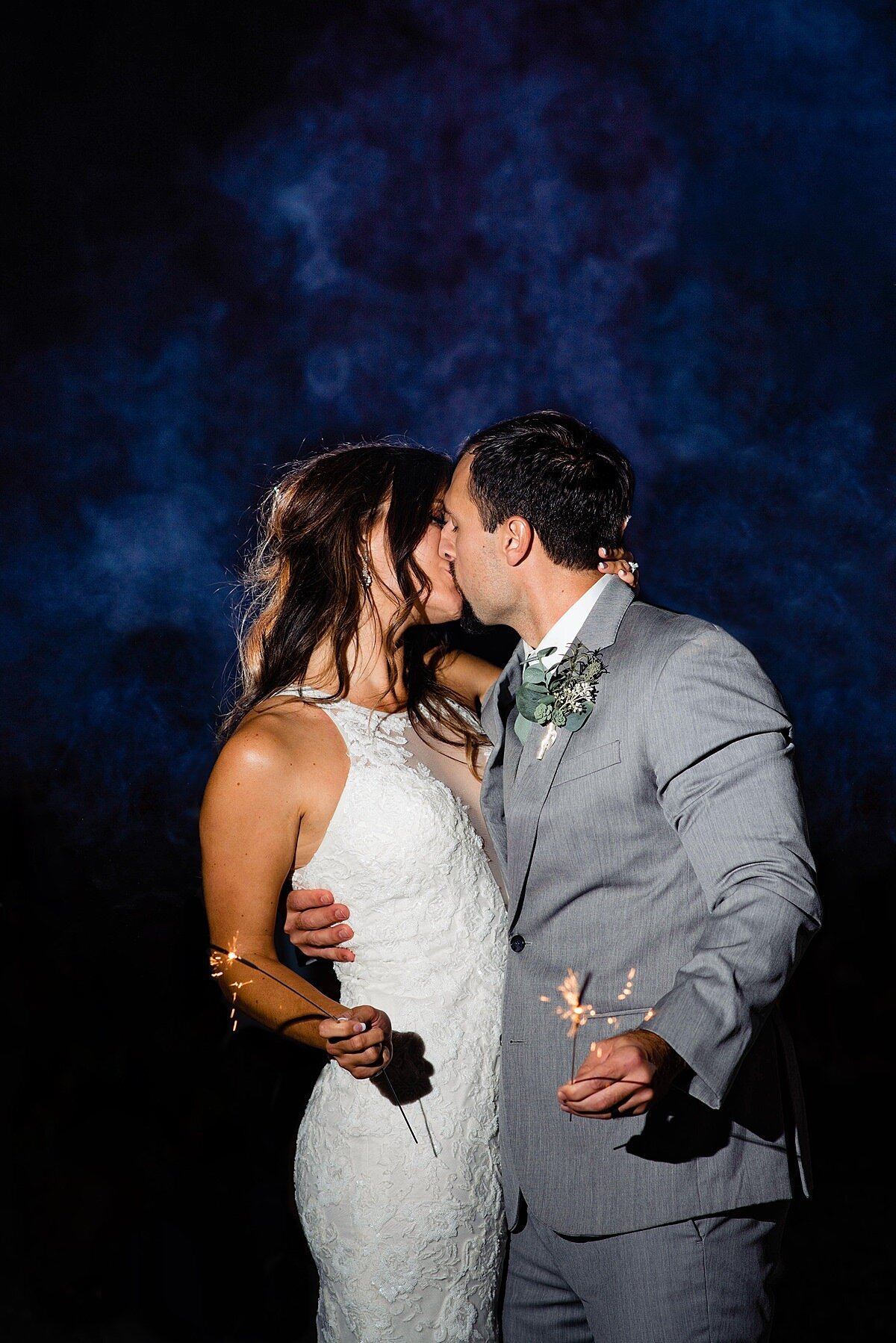 Bride and groom kissing while holding sparklers with smoke rising behind them