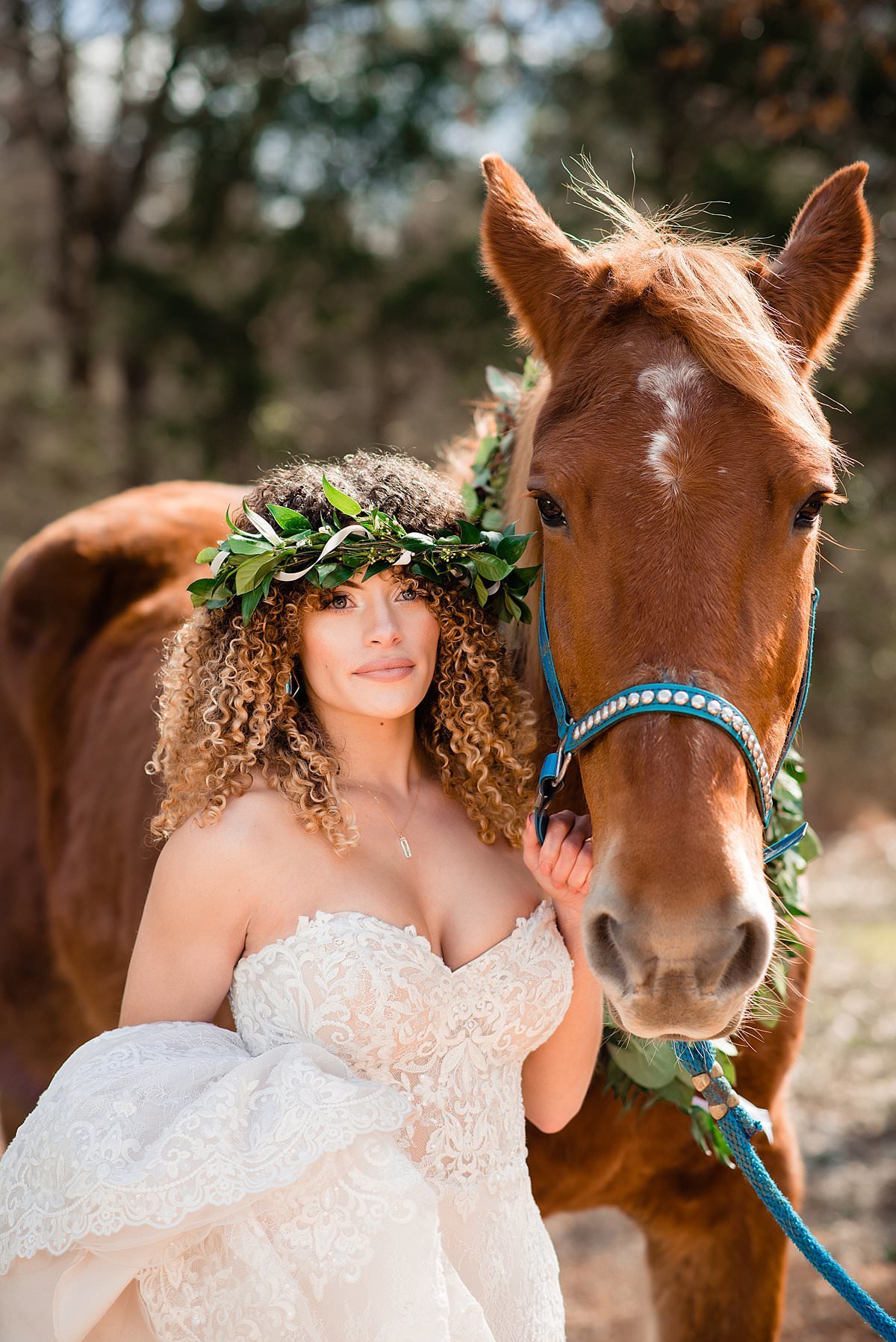 Bride wearing a lace sweetheart dress and greenery flower crown holding onto a beautiful brown horse