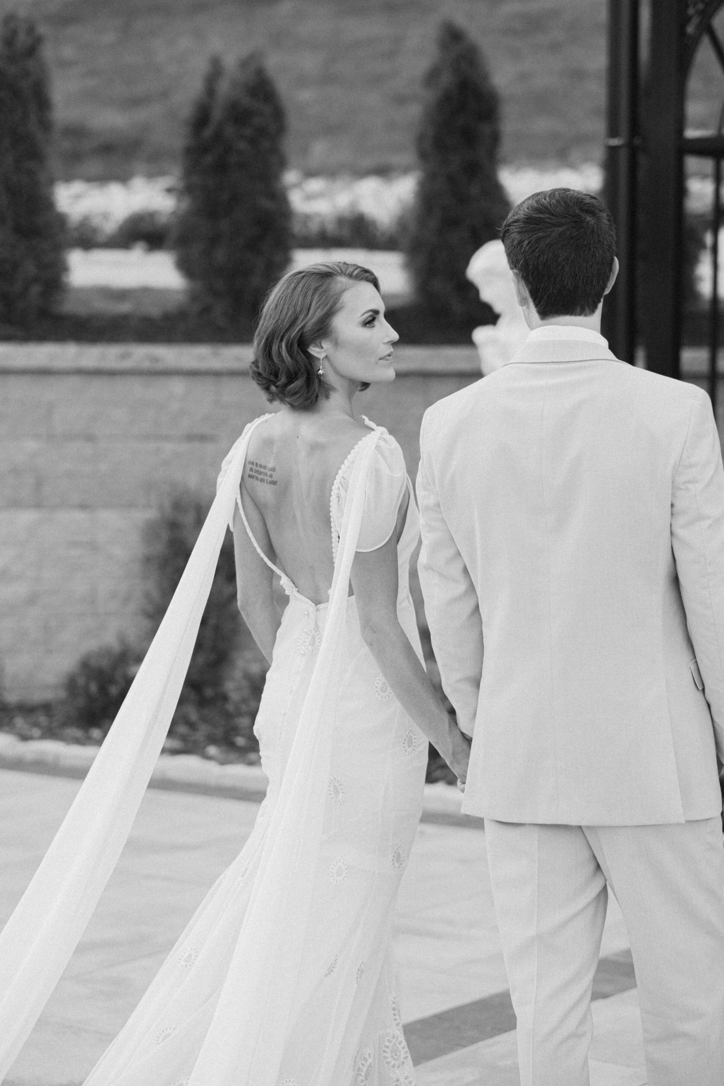 Black-and-white image of bride and groom walking hand in hand
