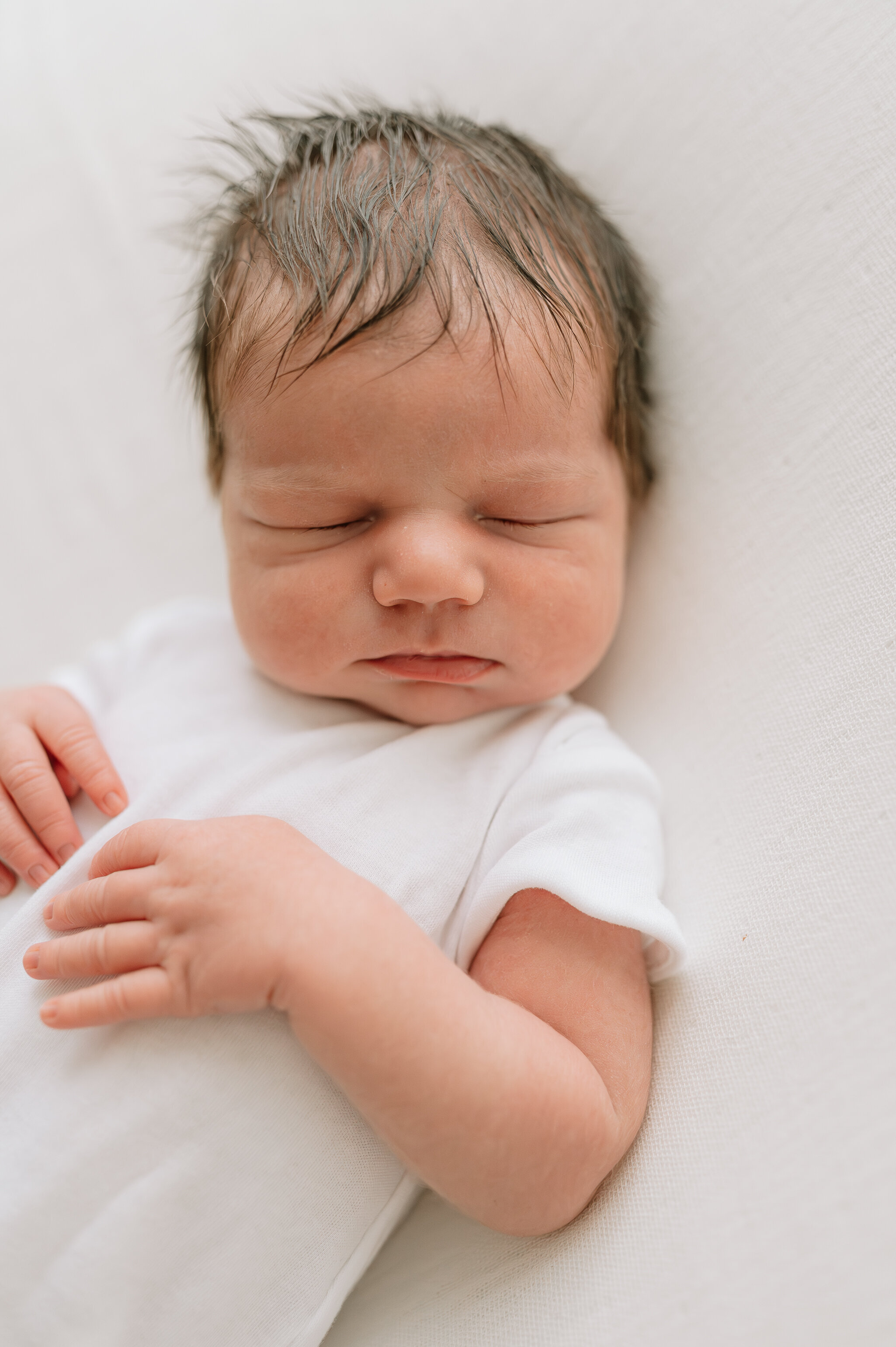 newborn baby boy with lovely hair and a white babygro