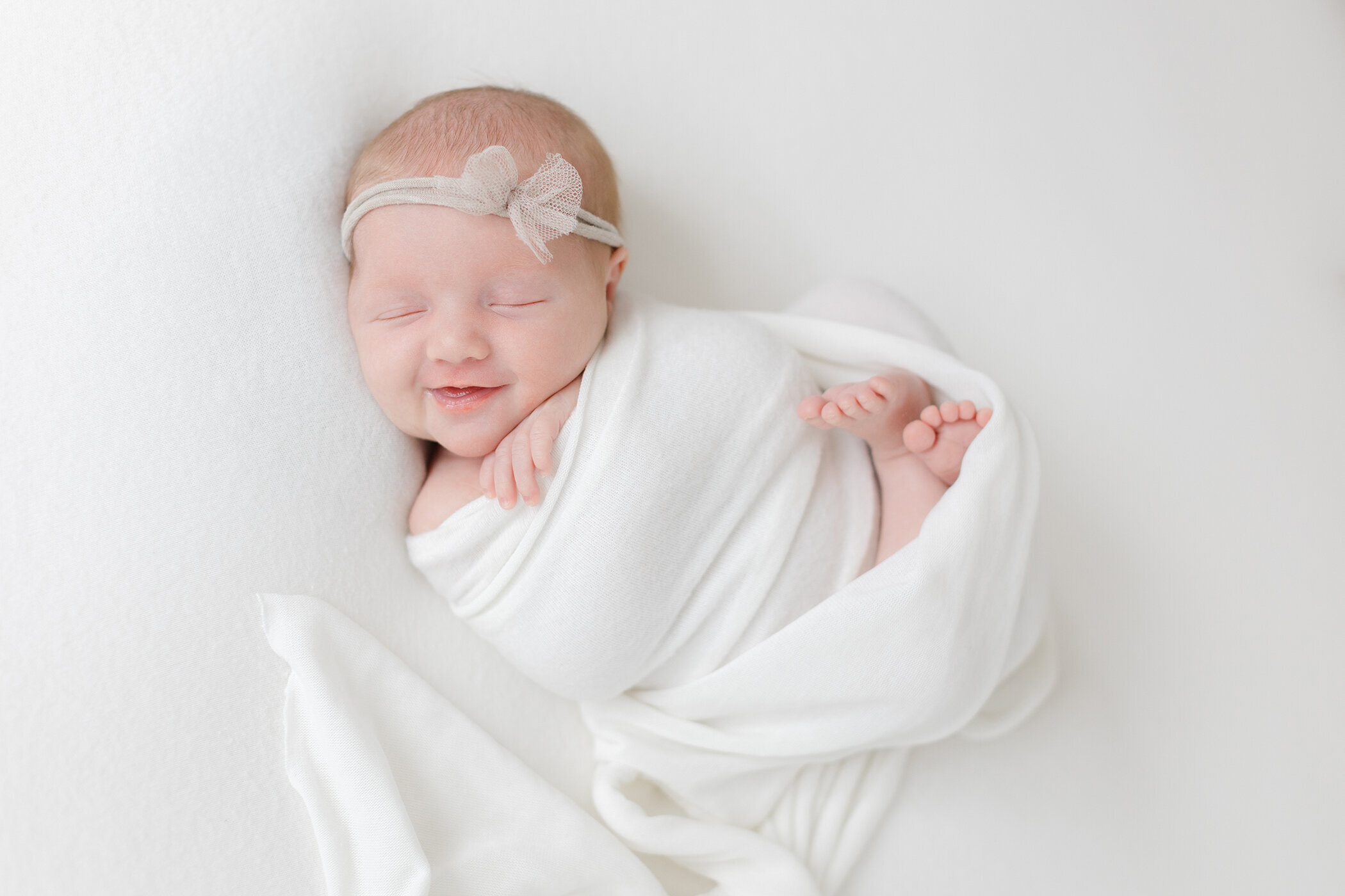 baby girl swaddled in white wrap smiling 
