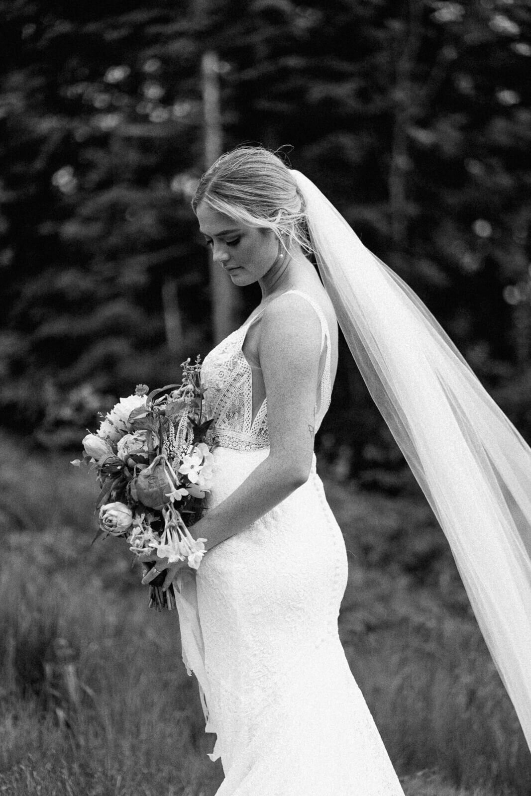 Black and white image of bride with veil looking at flower