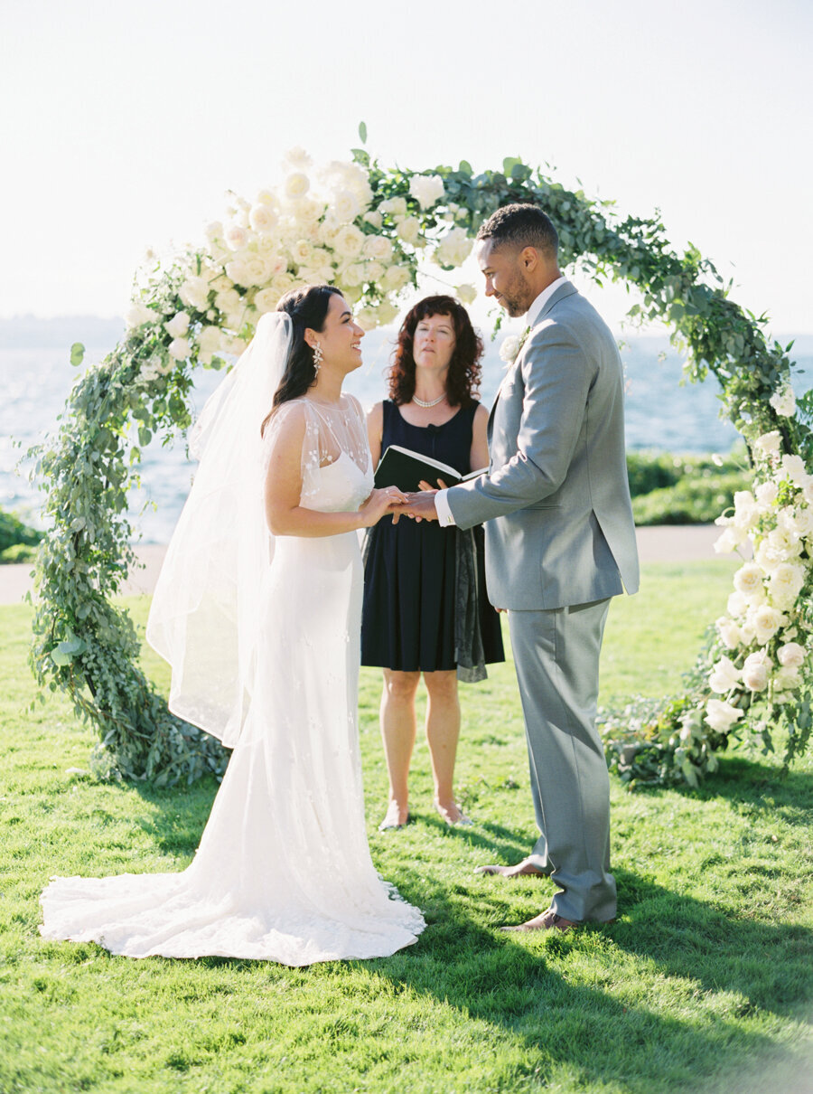 bride and groom holding hands facing each other at lakefront ceremony on grass
