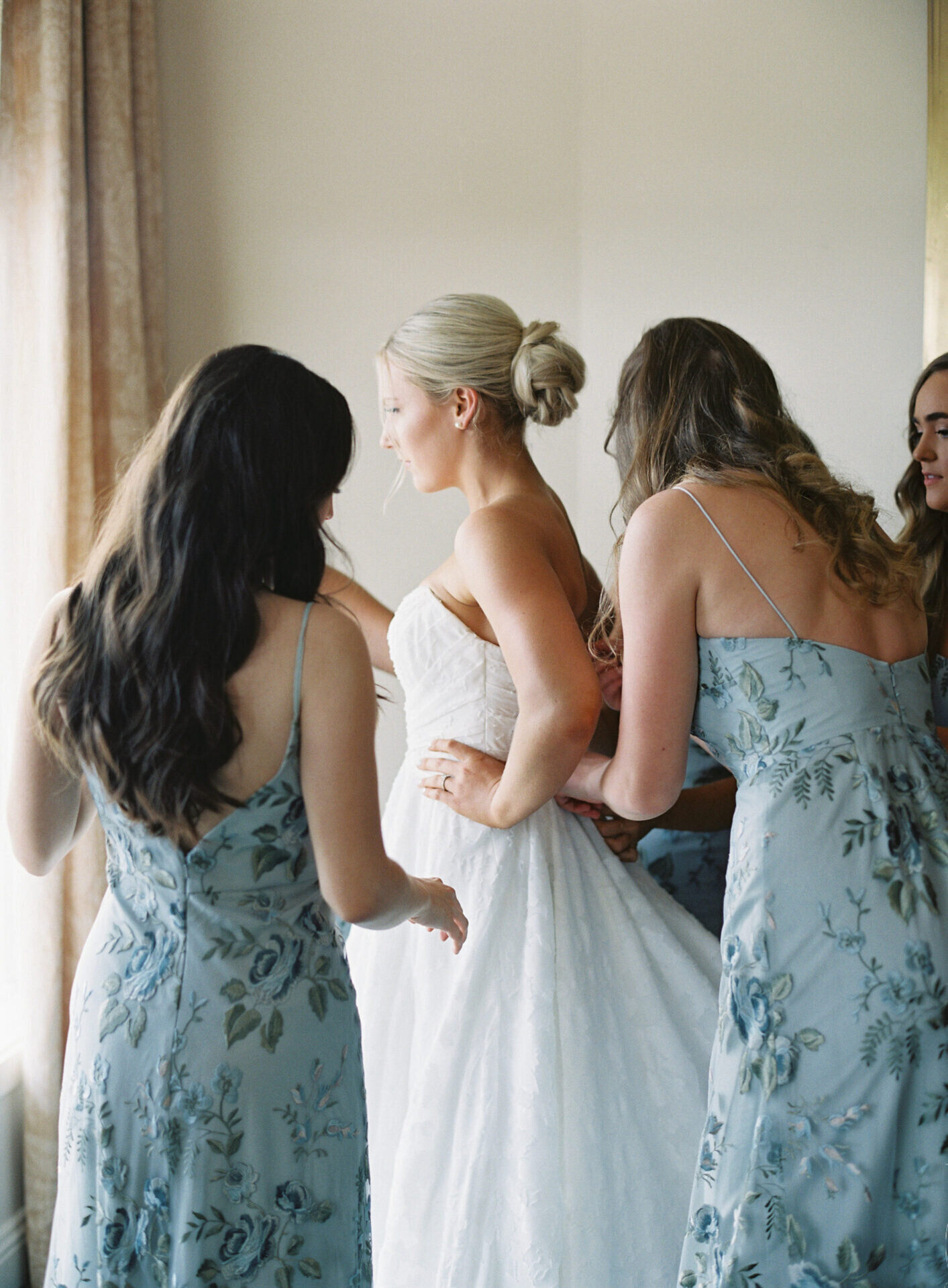 bride getting ready with her maids, zipping up dress