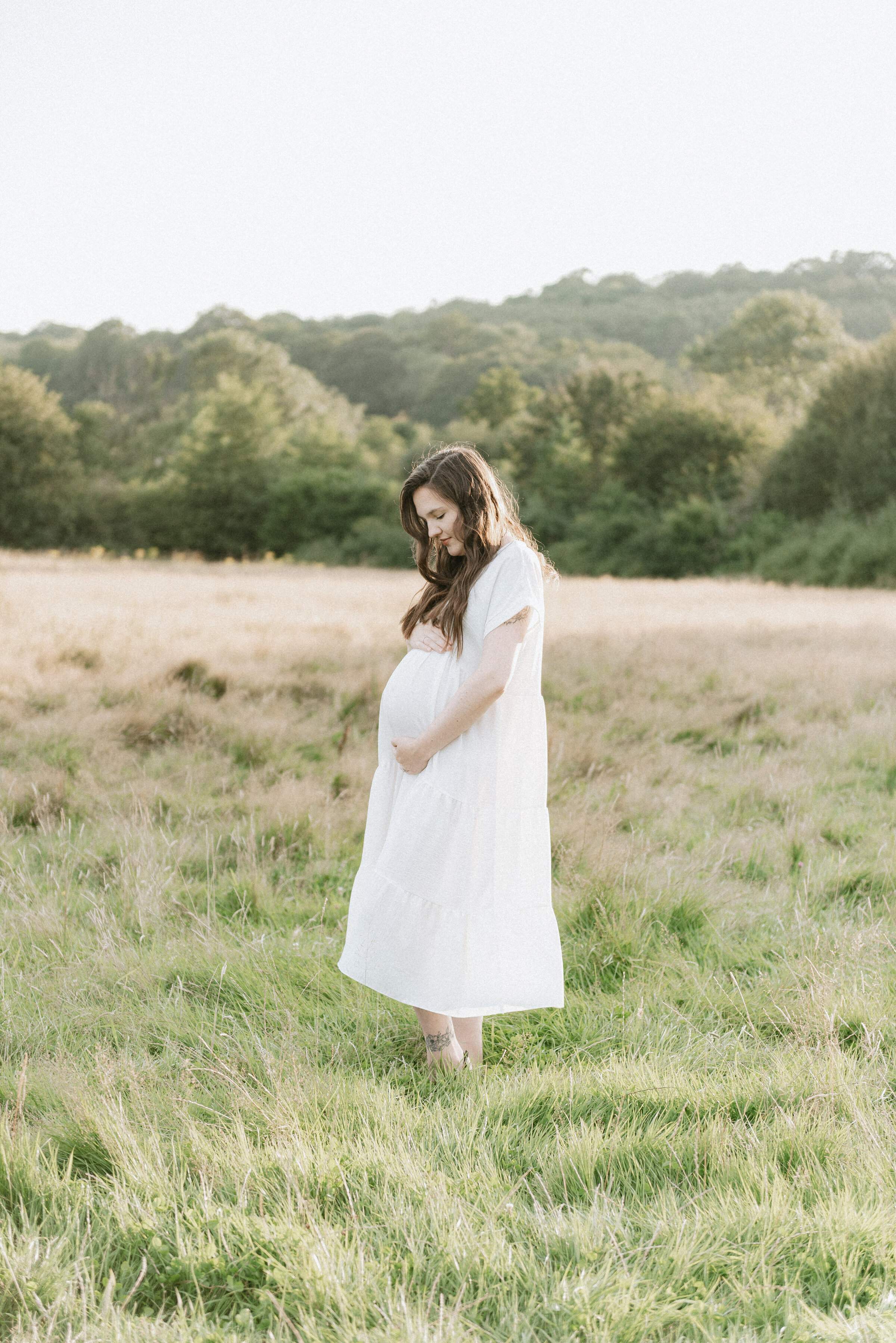 Pregnant women standing in a field at sunset at maternity photoshoot in Billingshurst