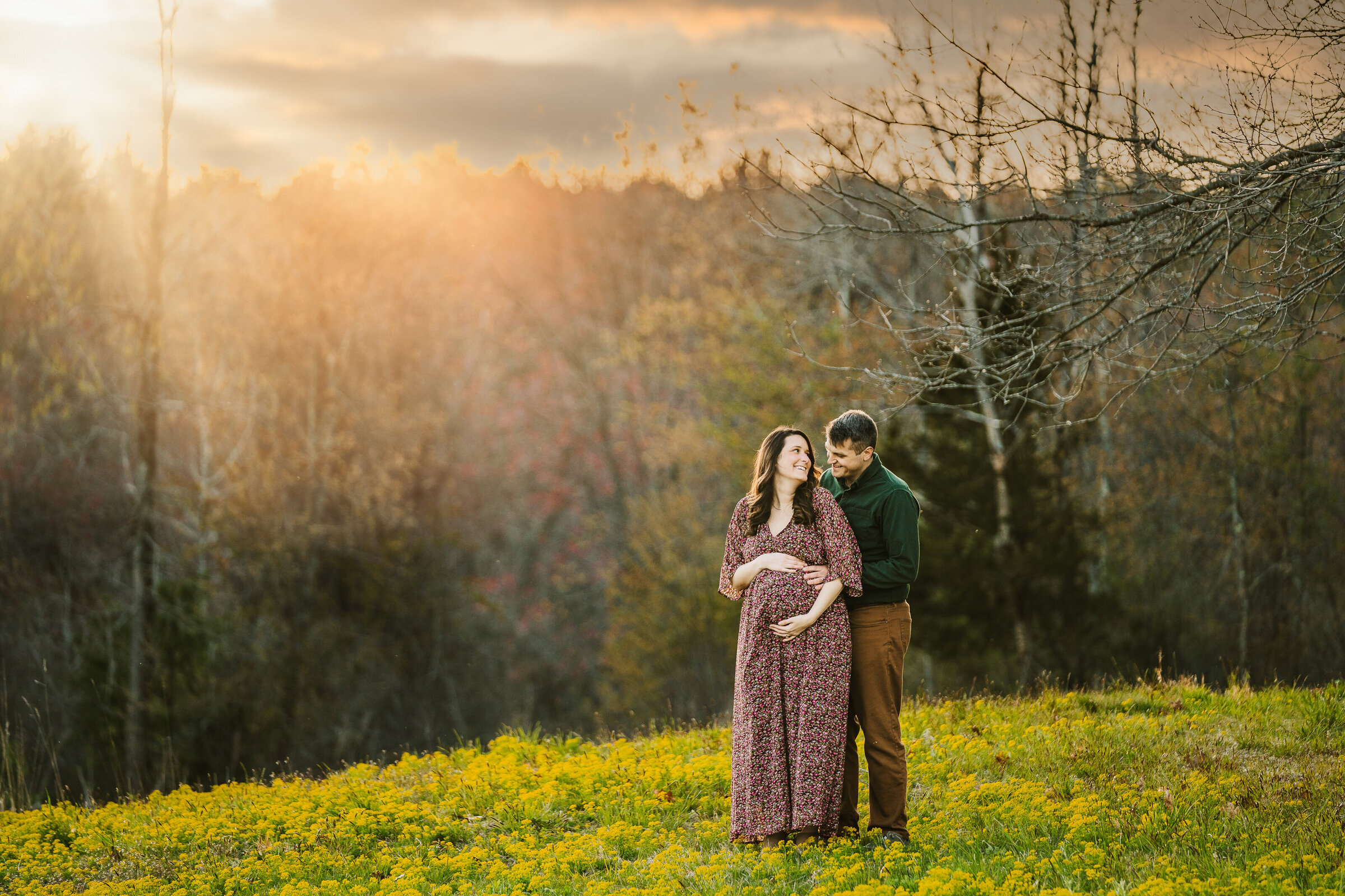 sun shines on pregnant couple in field of flowers
