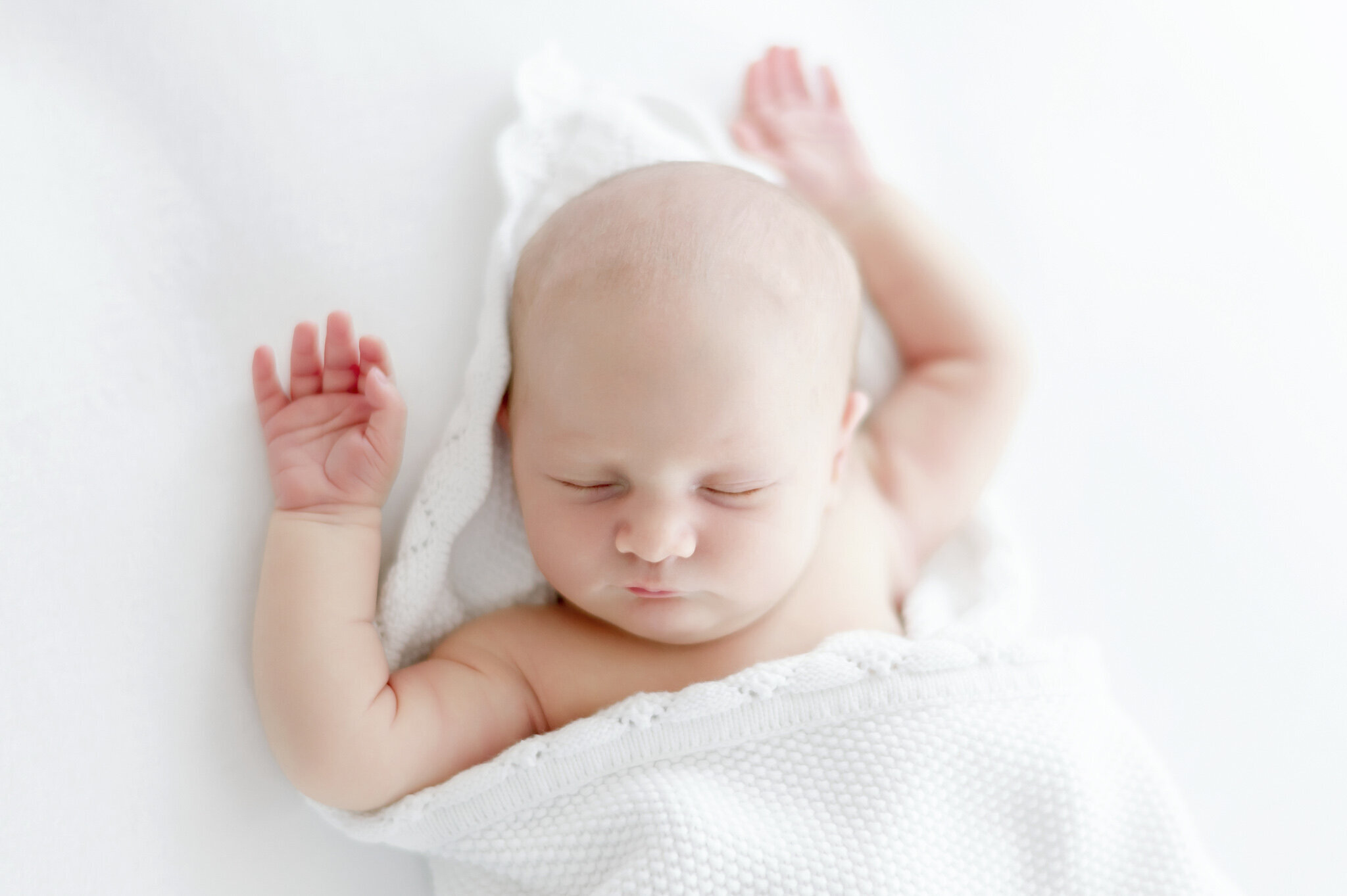 a newborn sleeps with hands up on a white bean bag  in Kristie Lloyd's Nashville newborn photography studio