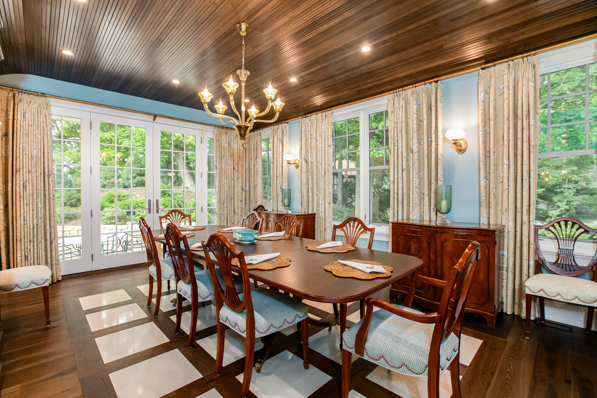 A luxurious dining room featuring rich wood ceilings, gold finishes, and an abundance of wood accents. The space is complemented by patterned curtains and custom flooring, creating a warm and inviting atmosphere.