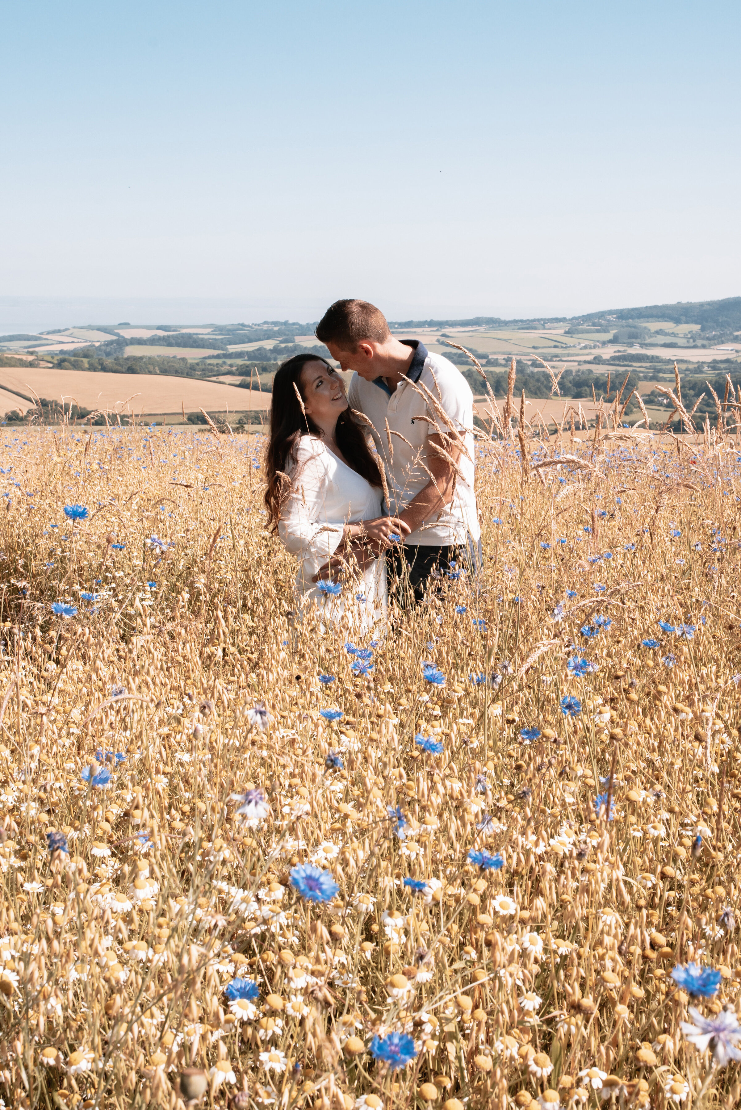 Man and woman gazing into each other’s eyes and laughing together in a field of wildflowers