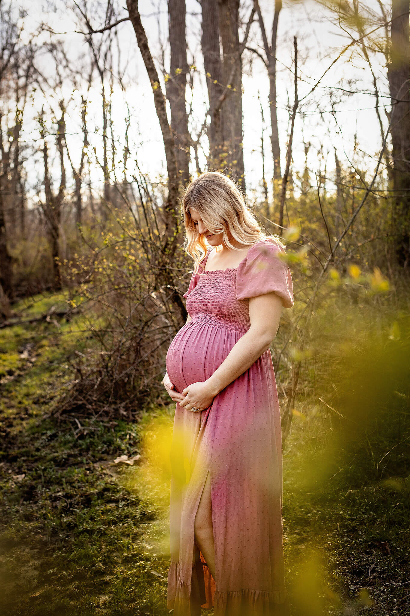 Pregnant women in pink dress in woods with sun shining behing her