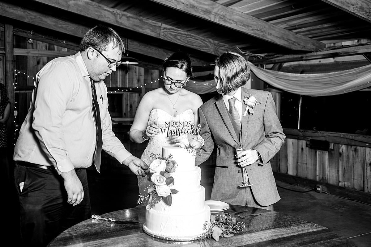 Black and white photo of Pat helping bride and groom cut their cake during reception