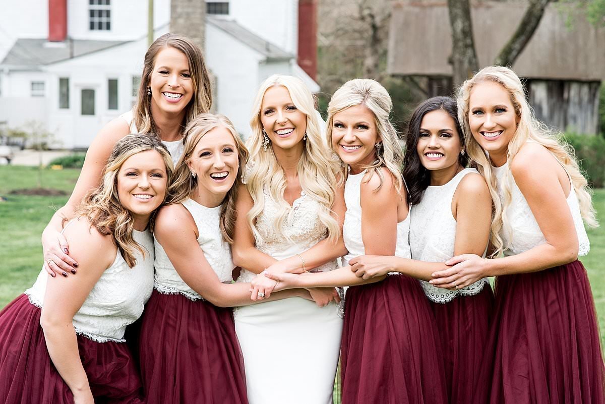 Group photo of bride and bridesmaids snuggled together with maroon and white accents