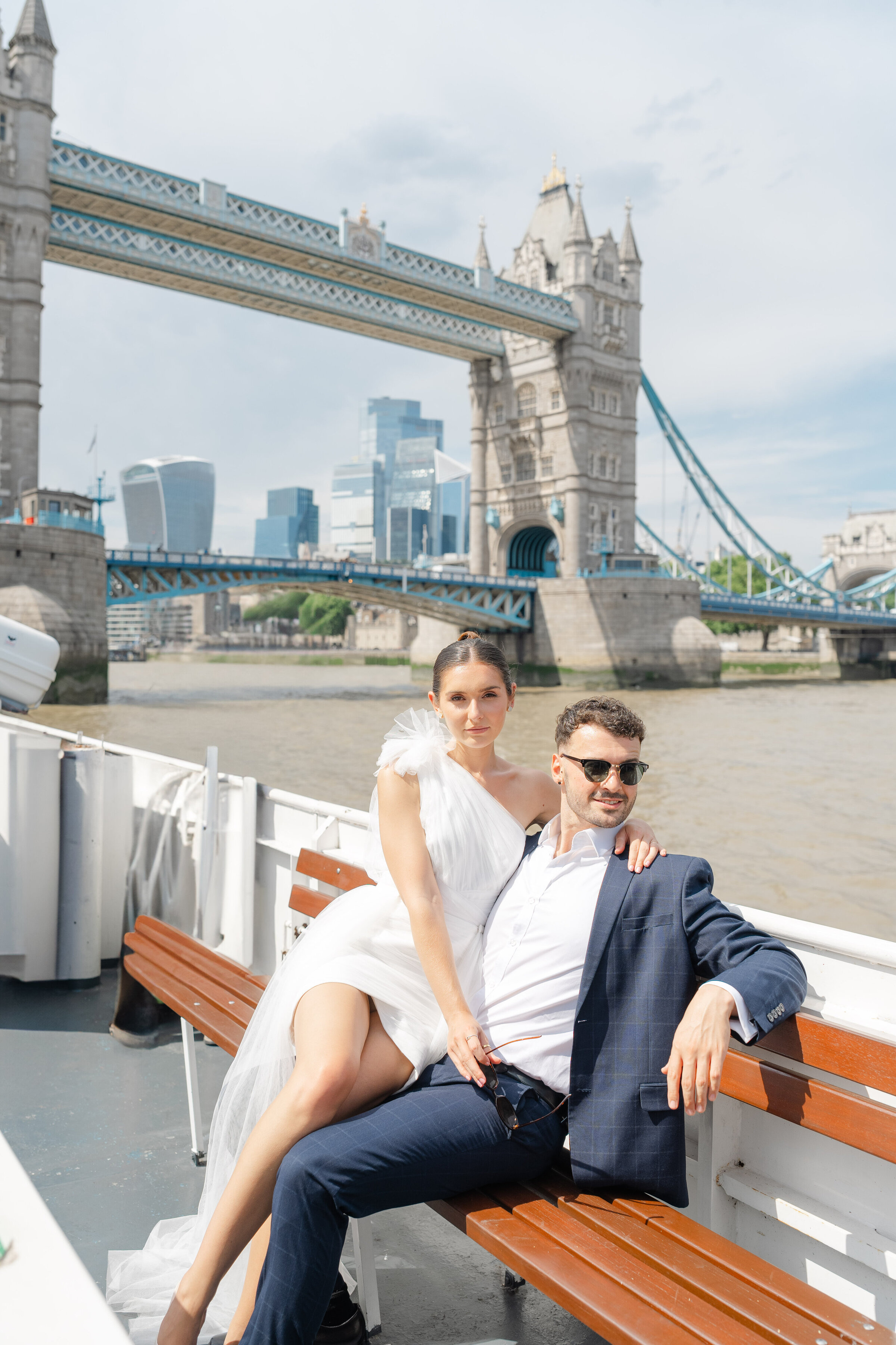 Bride and groom on a boat along the River Thames with Tower Bridge in the background – stylish London elopement by Chi Ramos Photography