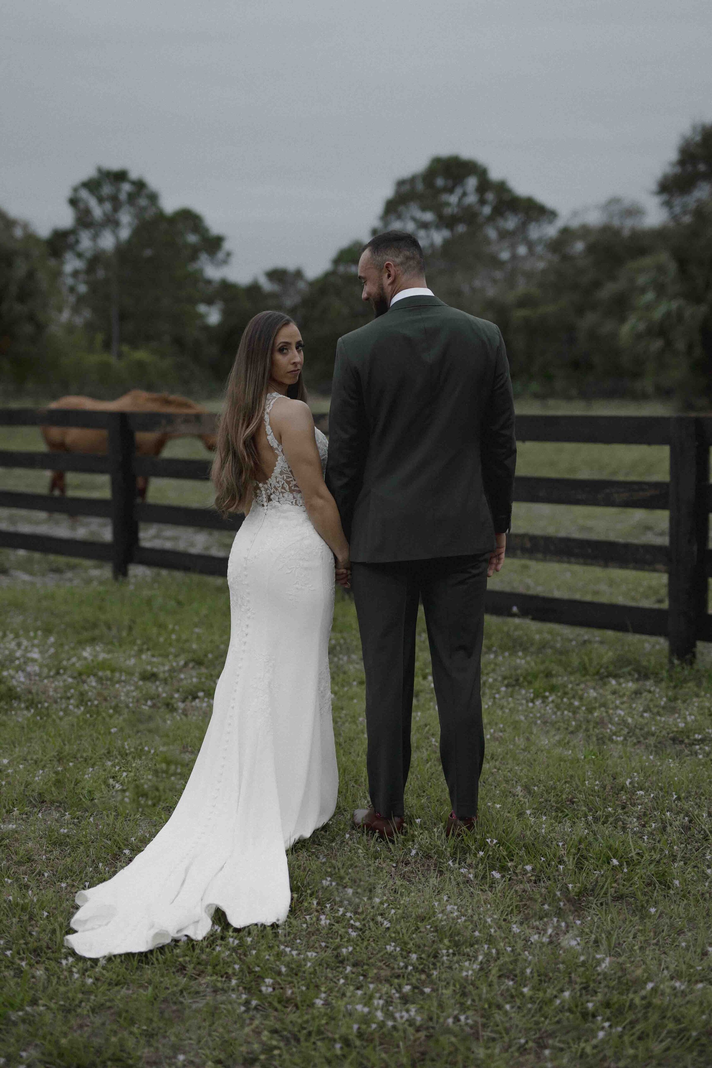Bride and groom standing in a field with a horse