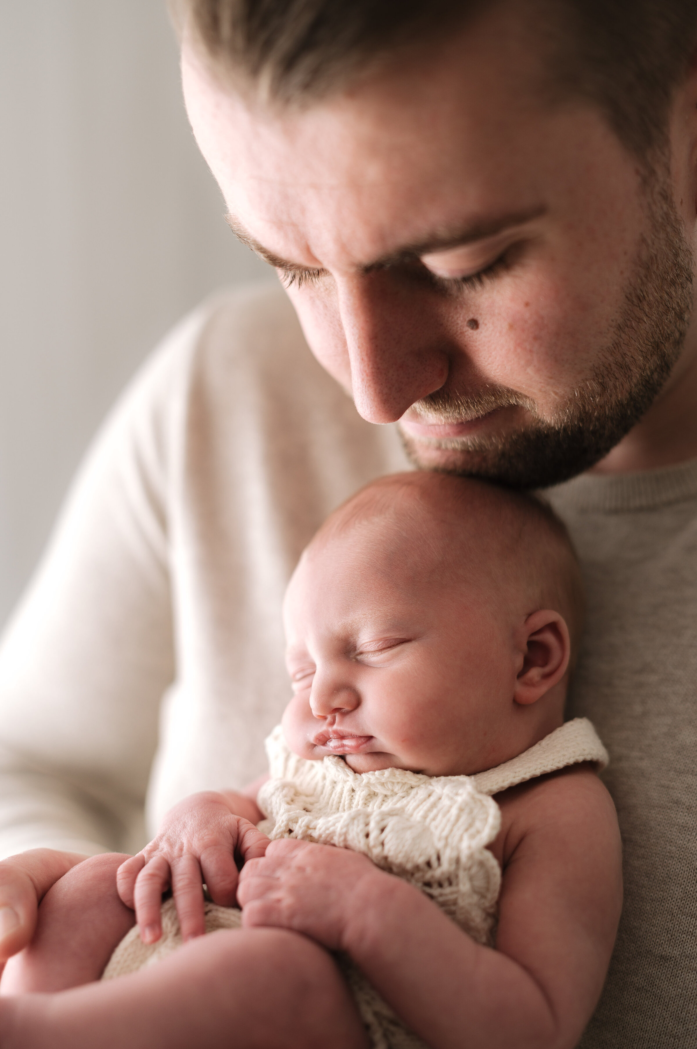 A father holding his newborn daughter under his chin at newborn photoshoot in Billingshurst