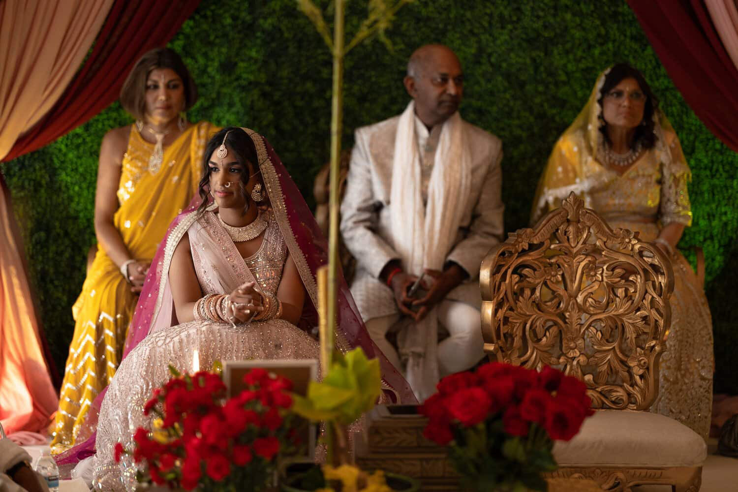 A bride in traditional South Asian attire sits beside her family during a cultural wedding ceremony at SoHo63, a Chandler wedding and event venue. Surrounded by vibrant colors, floral arrangements, and ornate seating, the scene highlights SoHo63’s ability to host beautifully diverse celebrations.