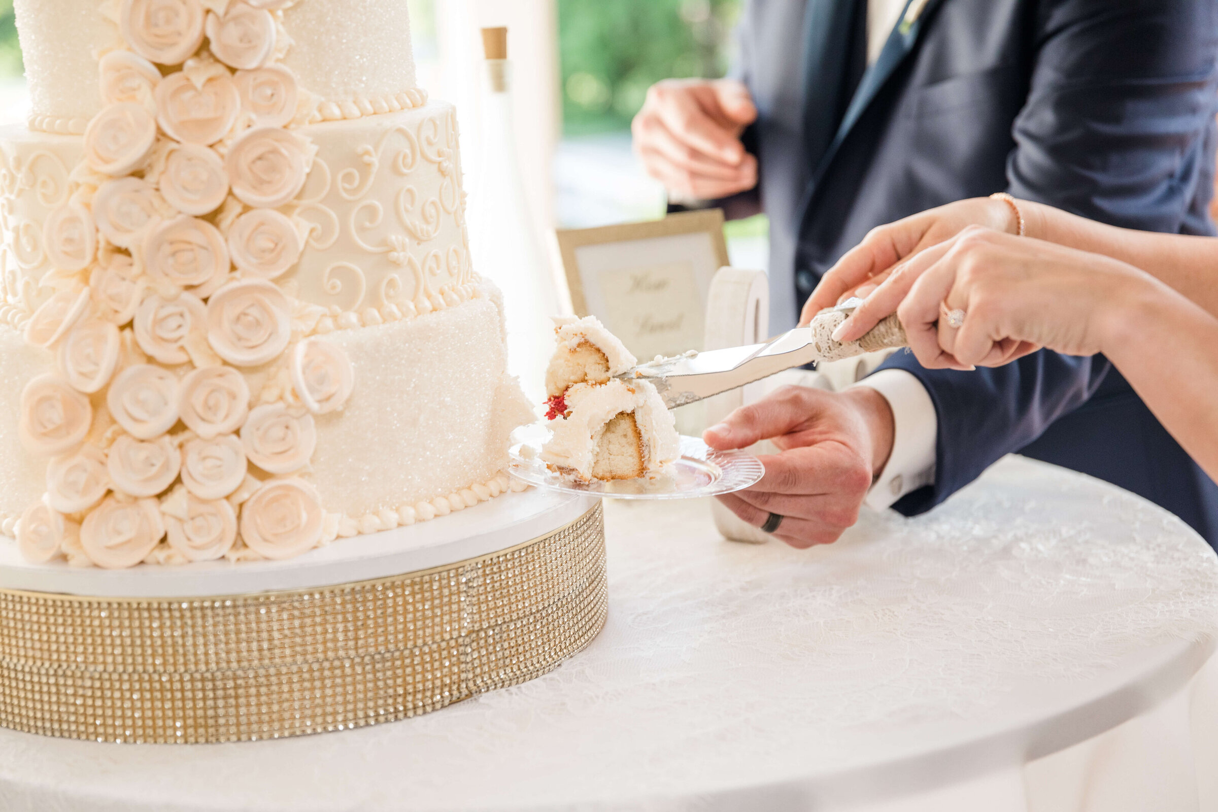 An up close photo of a bride and groom cutting their cake. The cake is light pink and the bride has the cake cut while the groom holds out a plate.