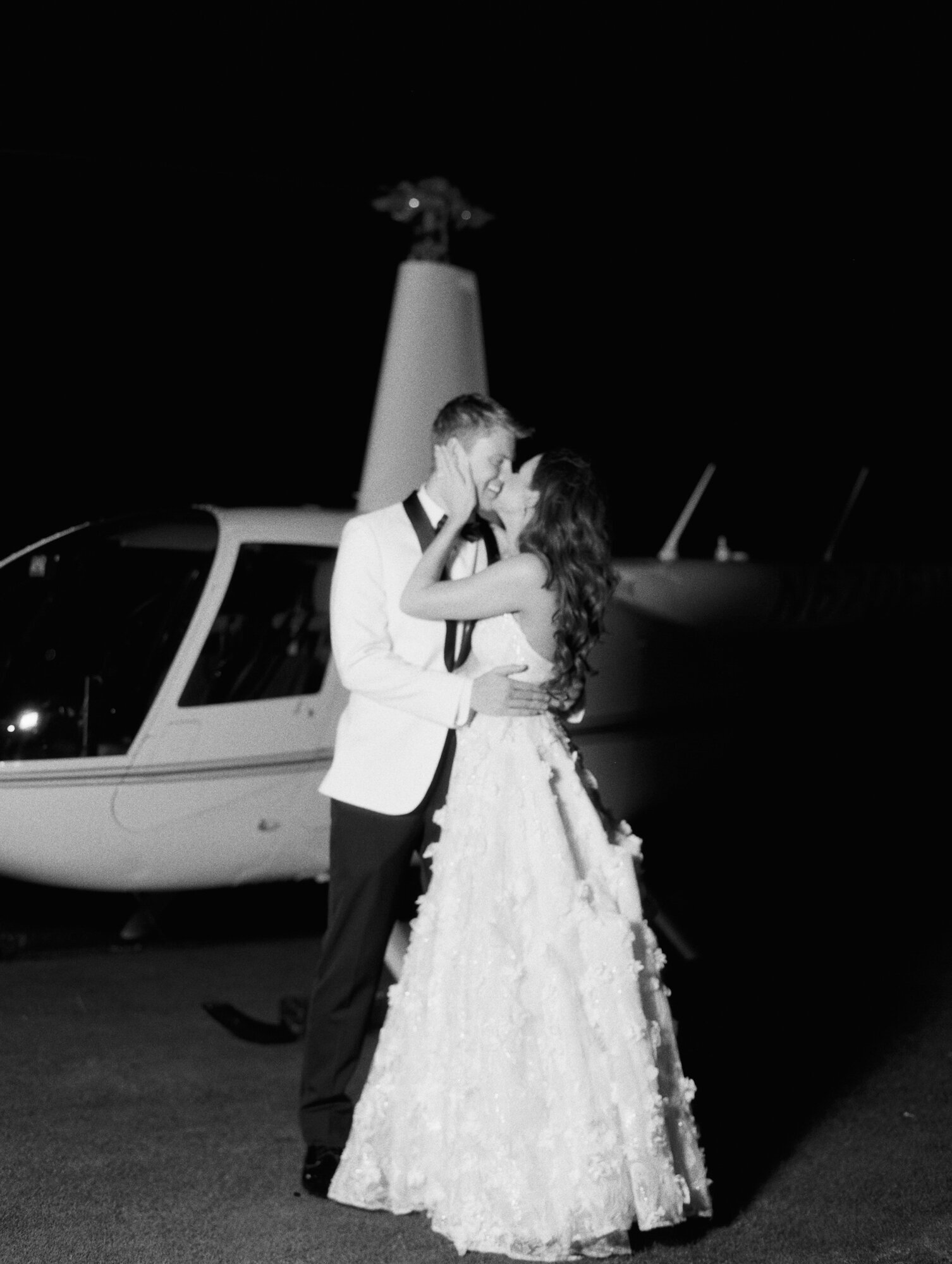 bride and groom kiss in front of helicopter black and white