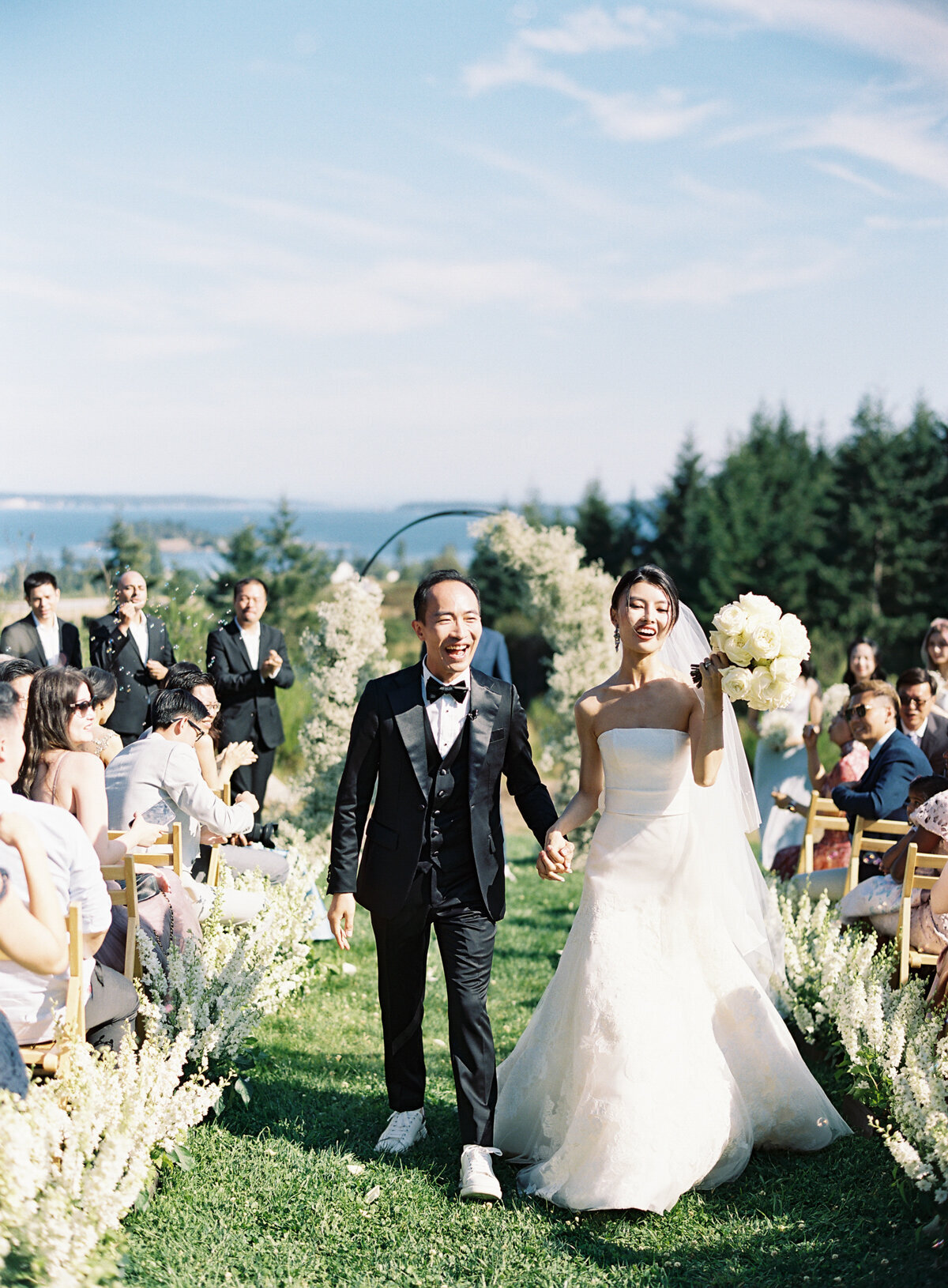 happy joyful bride and groom walk during processional on sunny outdoor day on grass