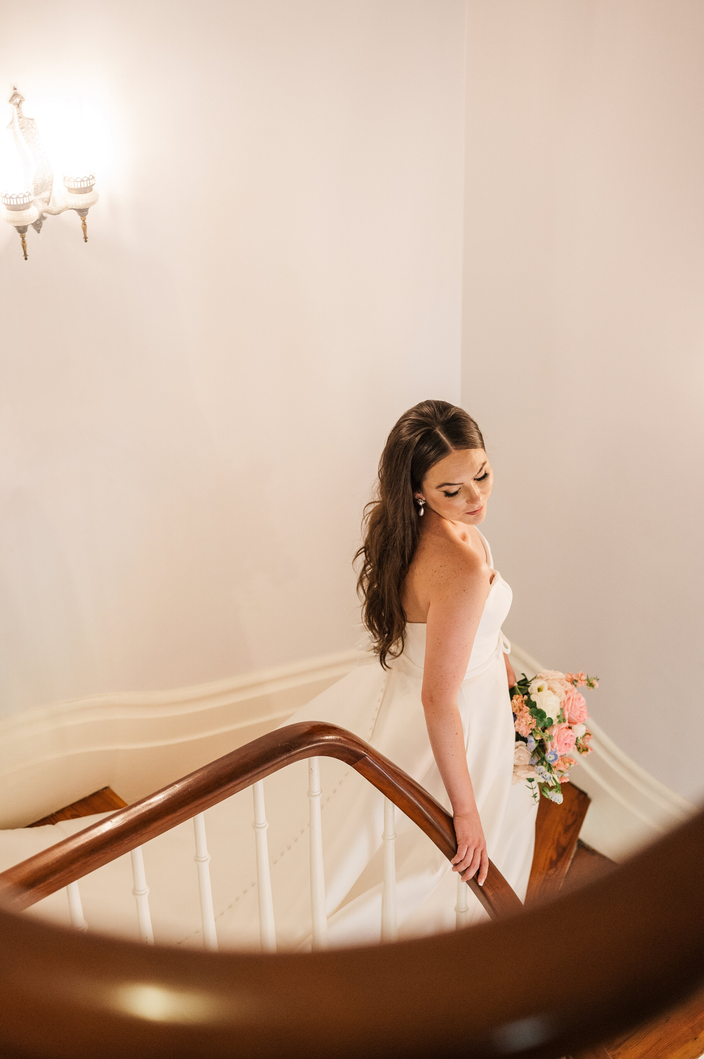 Bride looks over her shoulder as she walks down stairway at Ashford Acres Inn