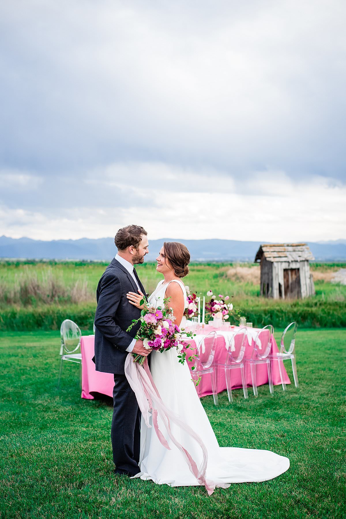 Bride and groom standing near outdoor reception table featuring hot pink linen with Montana mountains in background