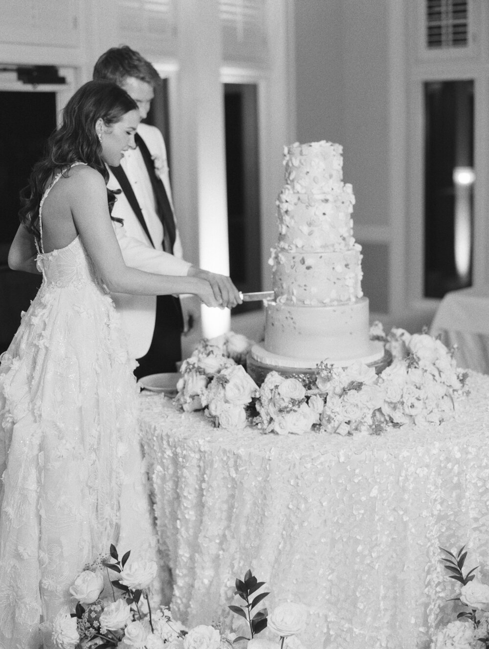 bw film photo of bride and groom cutting the cake