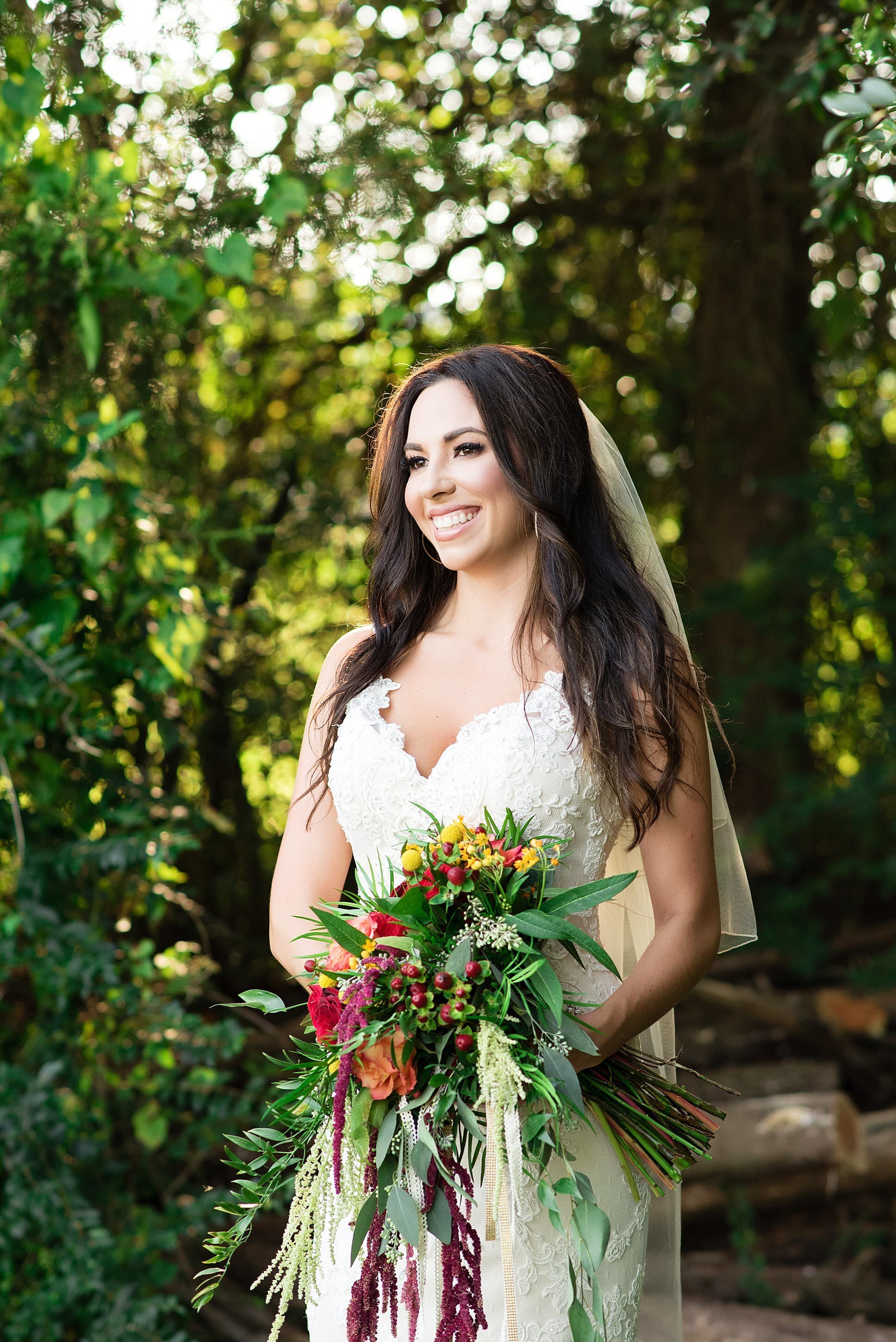 Bride holding colorful boho inspired bouquet smiling in a woodland setting