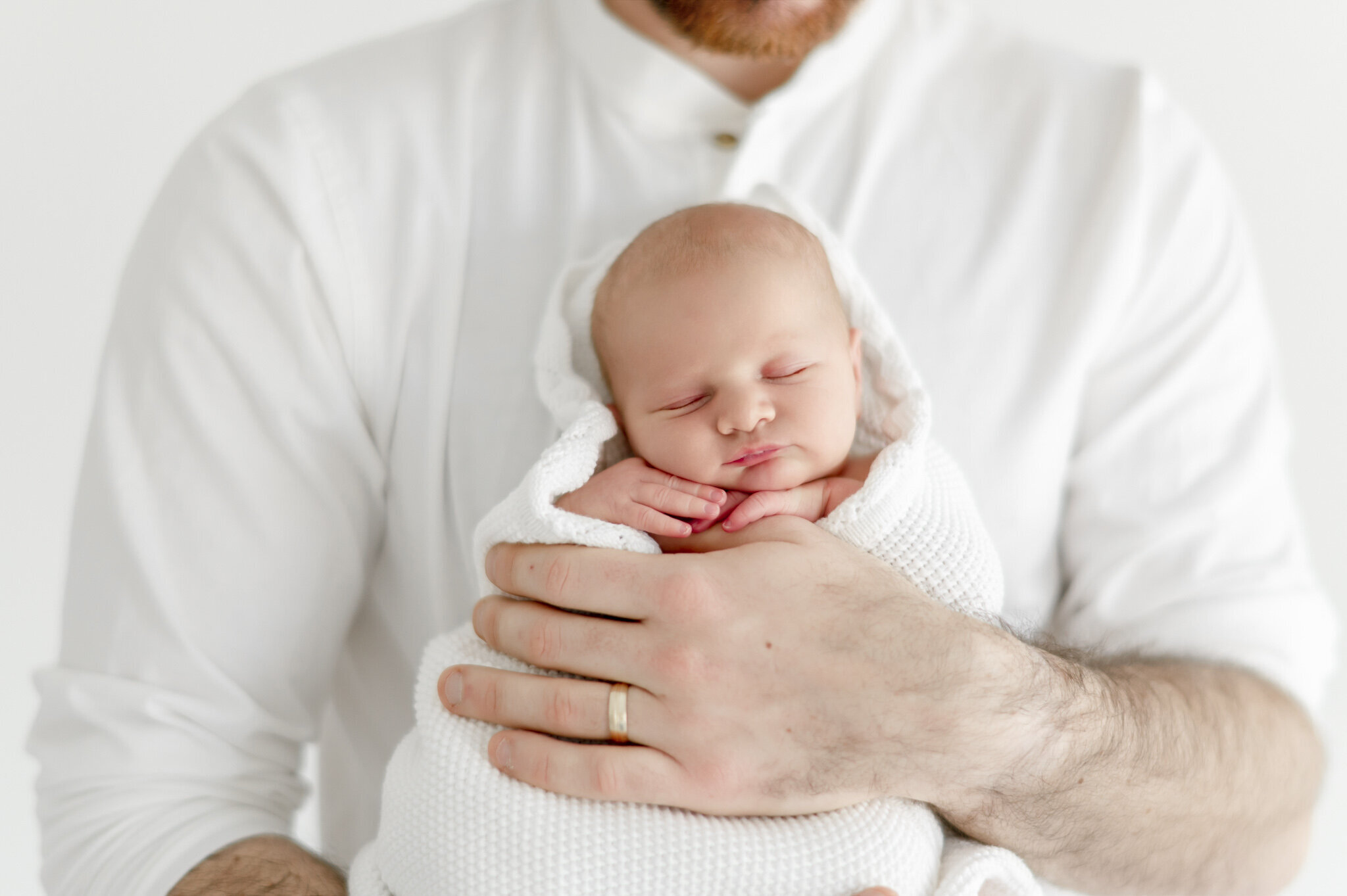 a father holds his sleeping newborn wrapped in a white blanket  in Kristie Lloyd's Nashville newborn photography studio