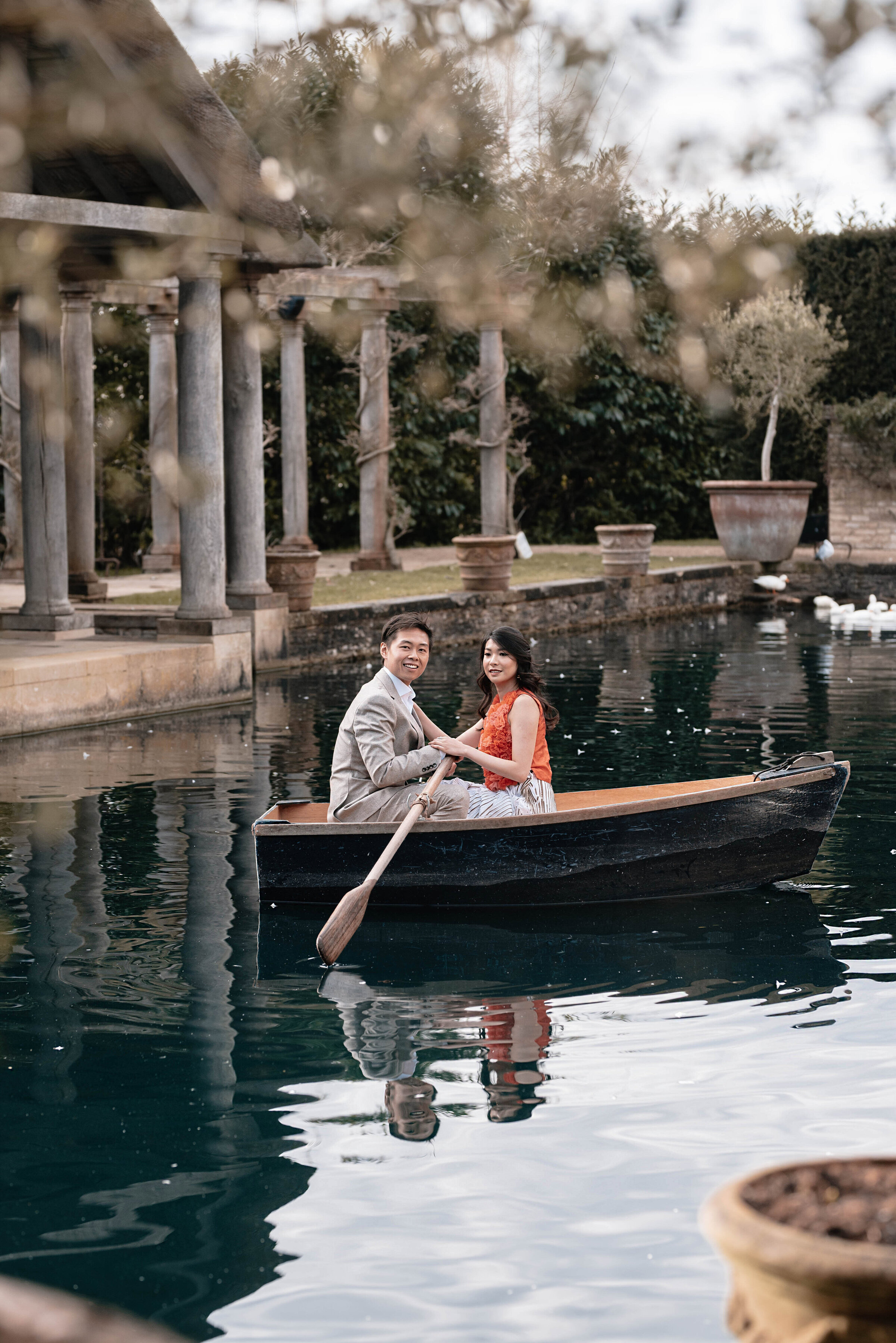 Man and woman on a small rowing boat in the middle of the pond at Euridge Manor wedding venue, smiling at the camera