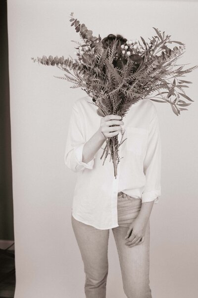 fallback shared on Invalid Date | a black and white photo of lorin husa standing with a boquet of greenery covering her fa...