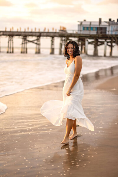 fallback shared on Invalid Date | Senior Girl at iconic Cocoa Beach Pier twirling white dress on the shoreline with water 