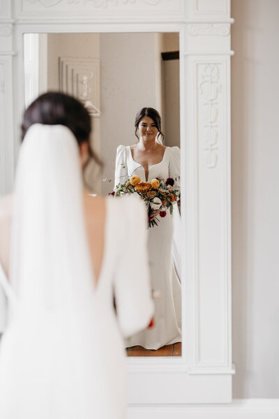 fallback shared on Invalid Date | A bride holds her bridal bouquet and looks at her reflection in the mirror