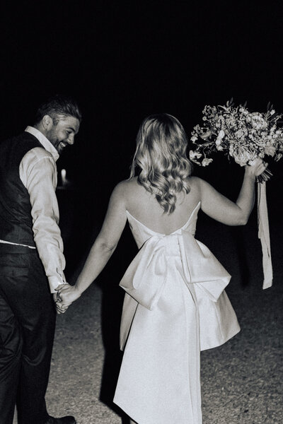 fallback shared on Invalid Date | A couple walk away from the camera hand in hand, the bride holds her bouquet above her h...