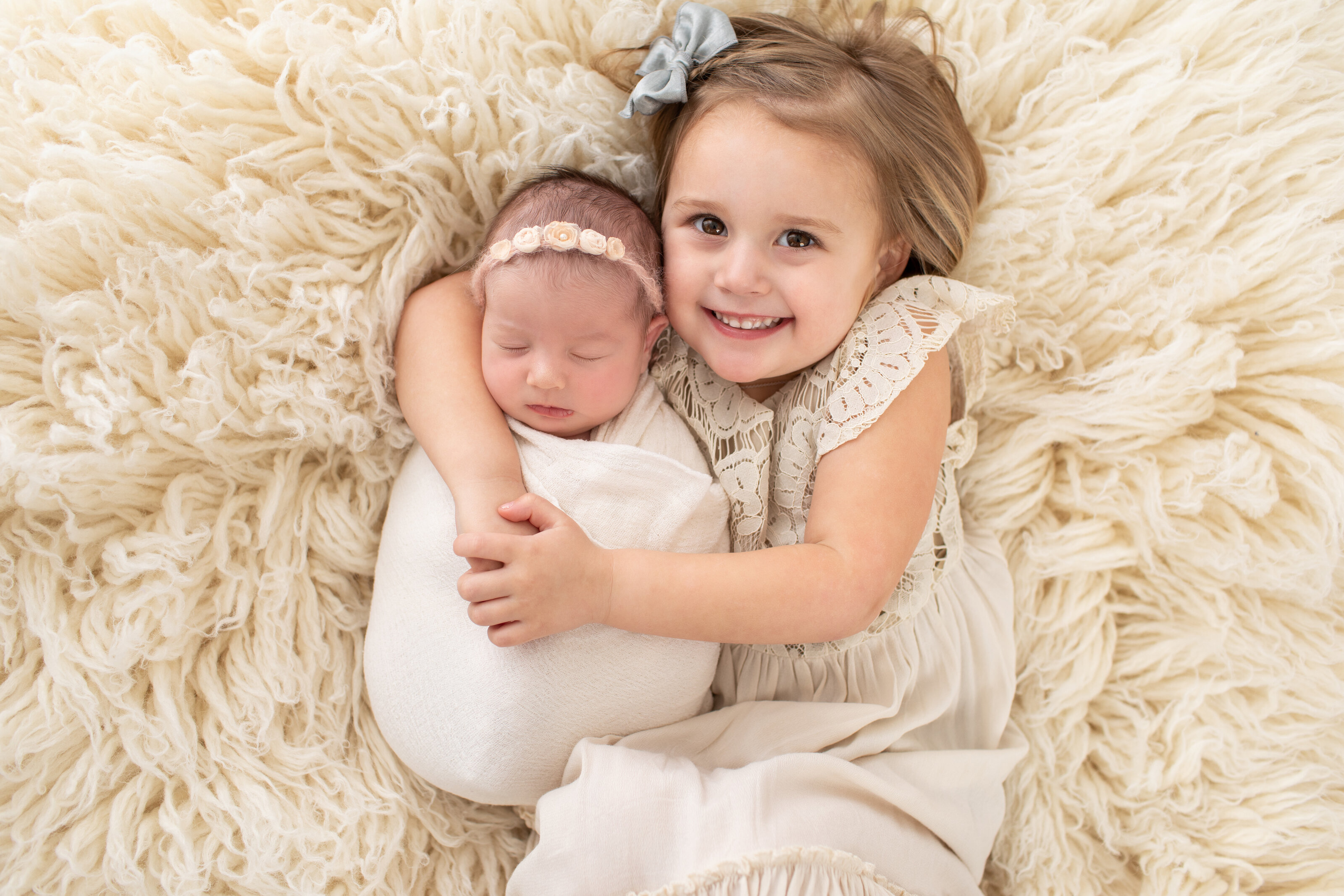 little girl holding newborn sister and smiling at the camera